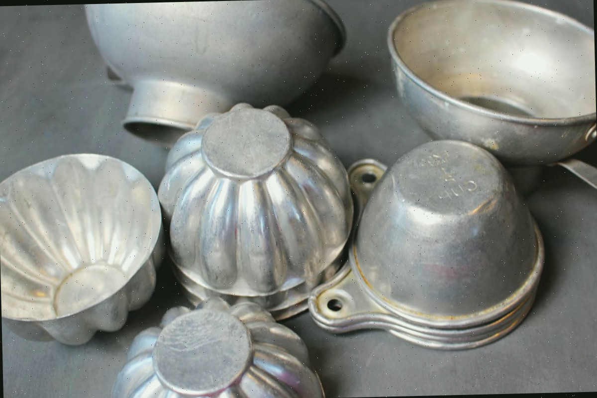 Pilhas de xícaras de medição de alumínio vintage, moldes de gelatina, funis e outros itens de cozinha.