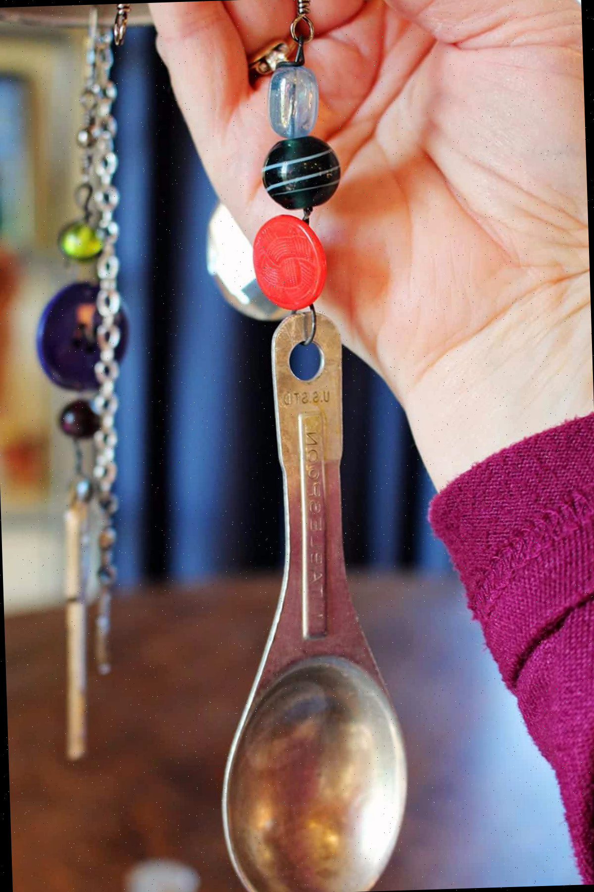 Uma mão segurando uma colher de medir vintage com um botão e contas enfiados em um fio.
