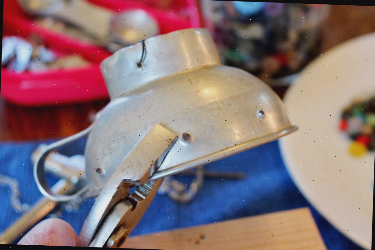Um funil vintage sendo segurado com um par de alicates, com furos perfurados na lateral.
