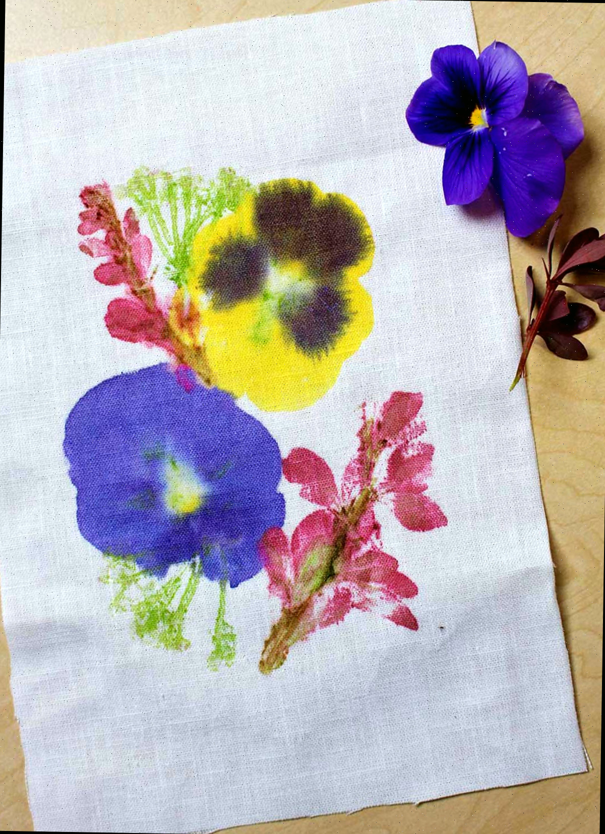 Um pedaço de tecido branco com impressões de flores marteladas sobre ele, acompanhadas por duas flores ao lado.