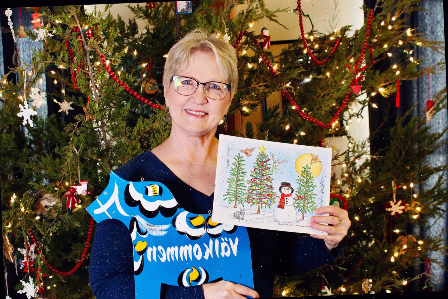 Foto da Nana segurando uma página de colorir de árvore de natal completa em frente à sua árvore de natal.