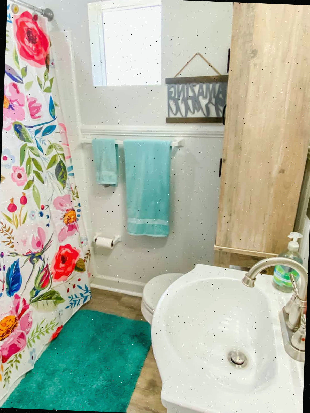 Banheiro pequeno com cortina de chuveiro floral e toalhas aqua