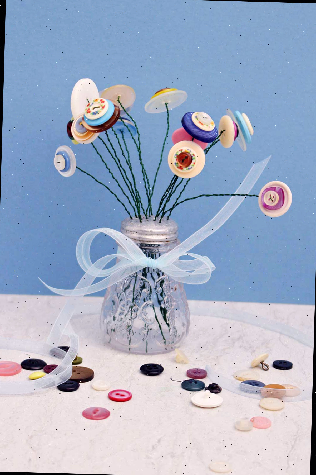 um saleiro repleto de flores de botão com uma fita amarrada ao redor, em um fundo azul.