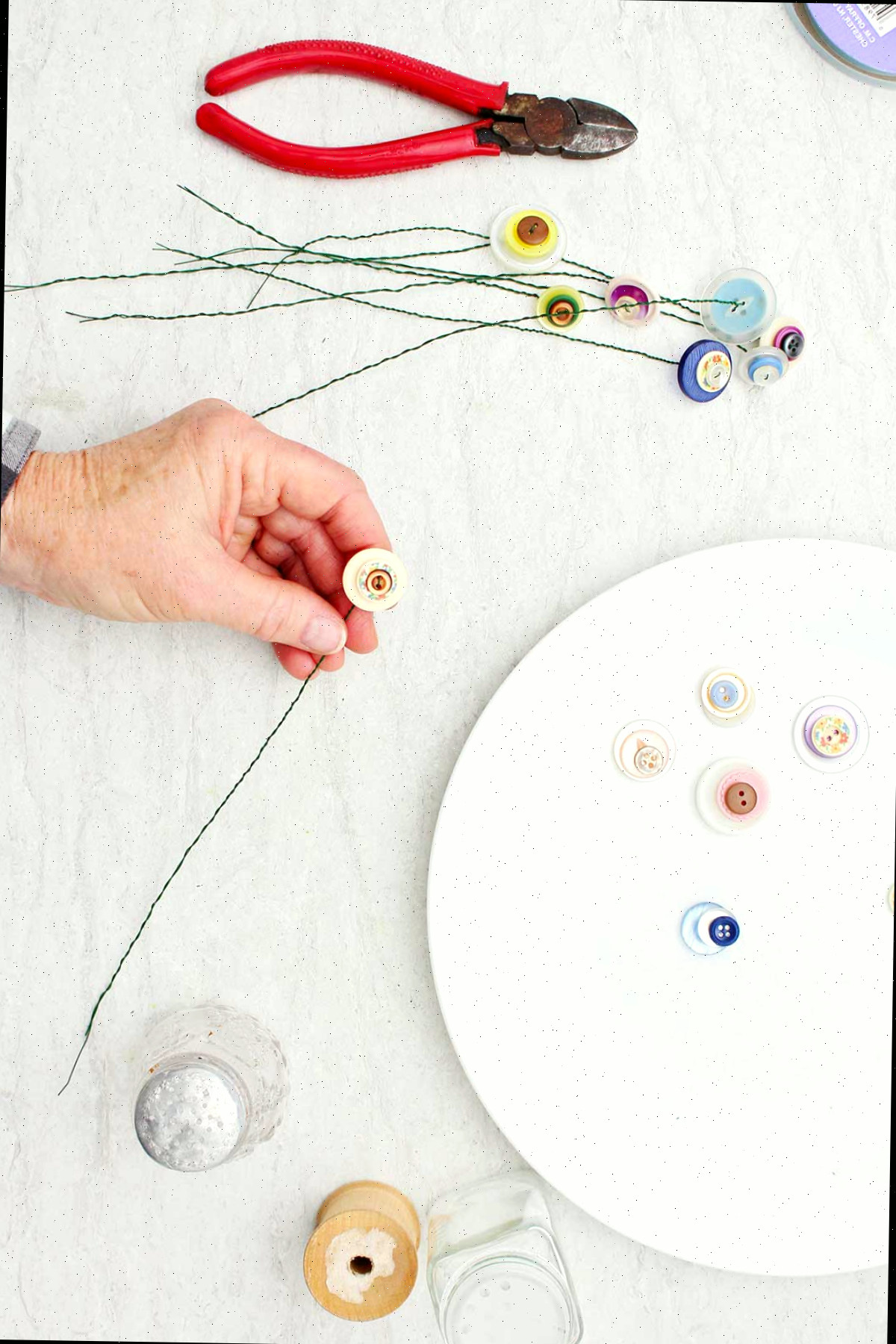 Uma pessoa segurando um caule terminado de uma flor de botão com outros materiais ao redor.