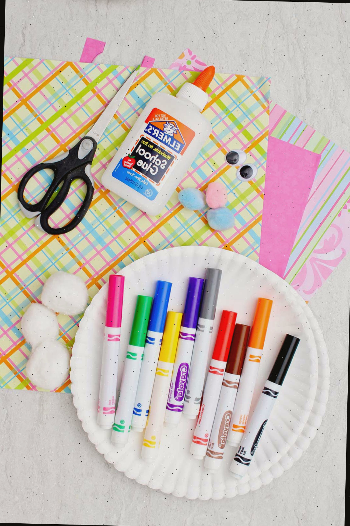 Um prato com canetinhas, tesoura, cola, papel decorativo, olhos móveis e bolinhas de algodão.
