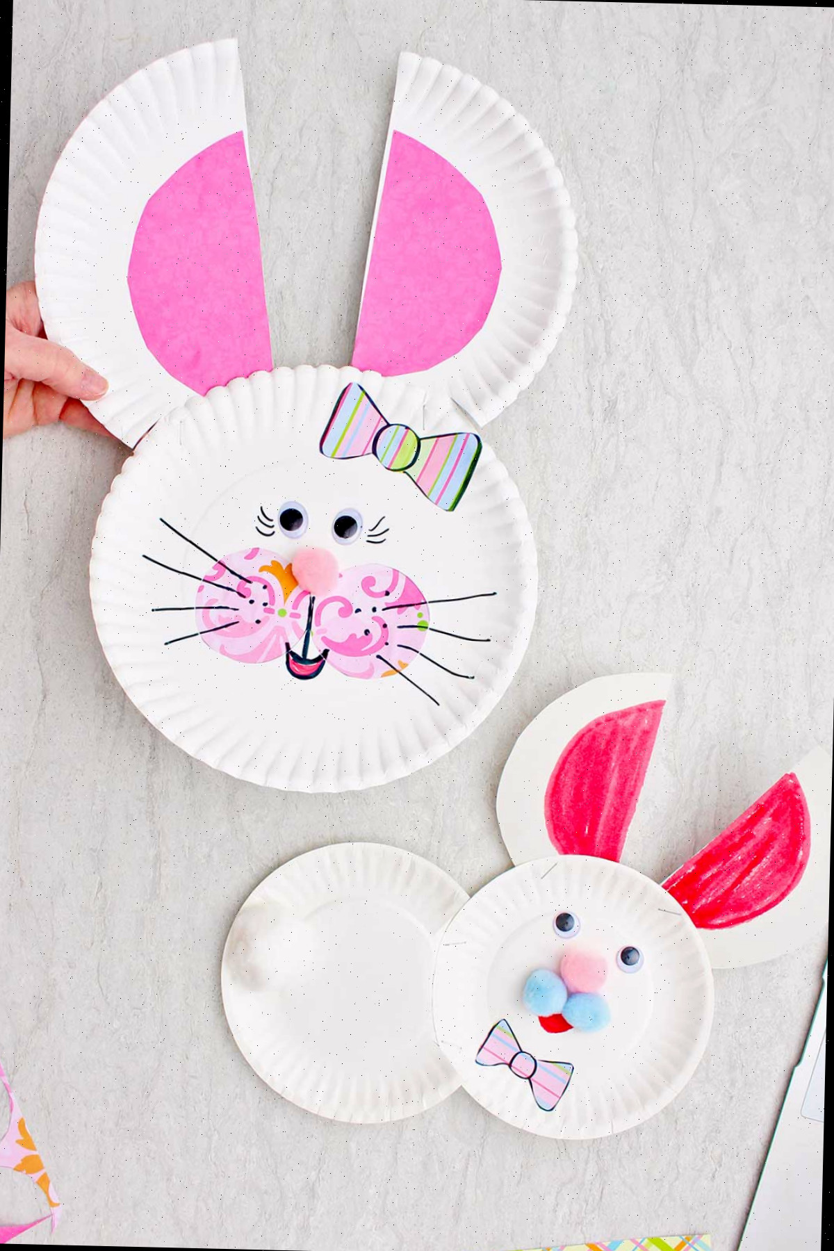 Indivíduo segurando uma face de coelhinho feita de papel, com outro coelhinho de papel próximo.