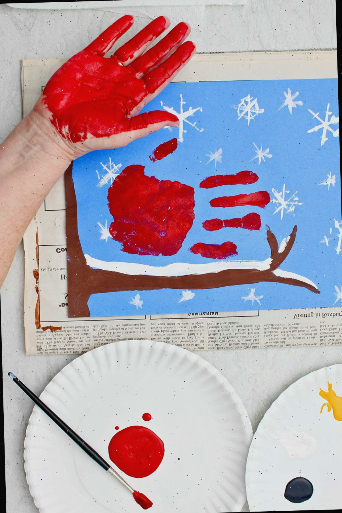 Pessoa mostrando a mão pintada de vermelho após carimbá-la em seu papel de construção de cena de inverno.