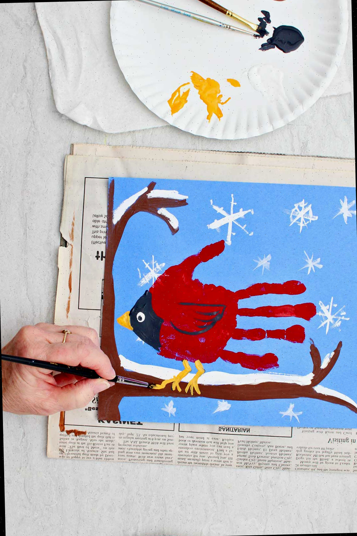 Pessoa pintando os toques finais em uma obra de arte de impressão de mão de cardeal descansando em um galho coberto de neve.