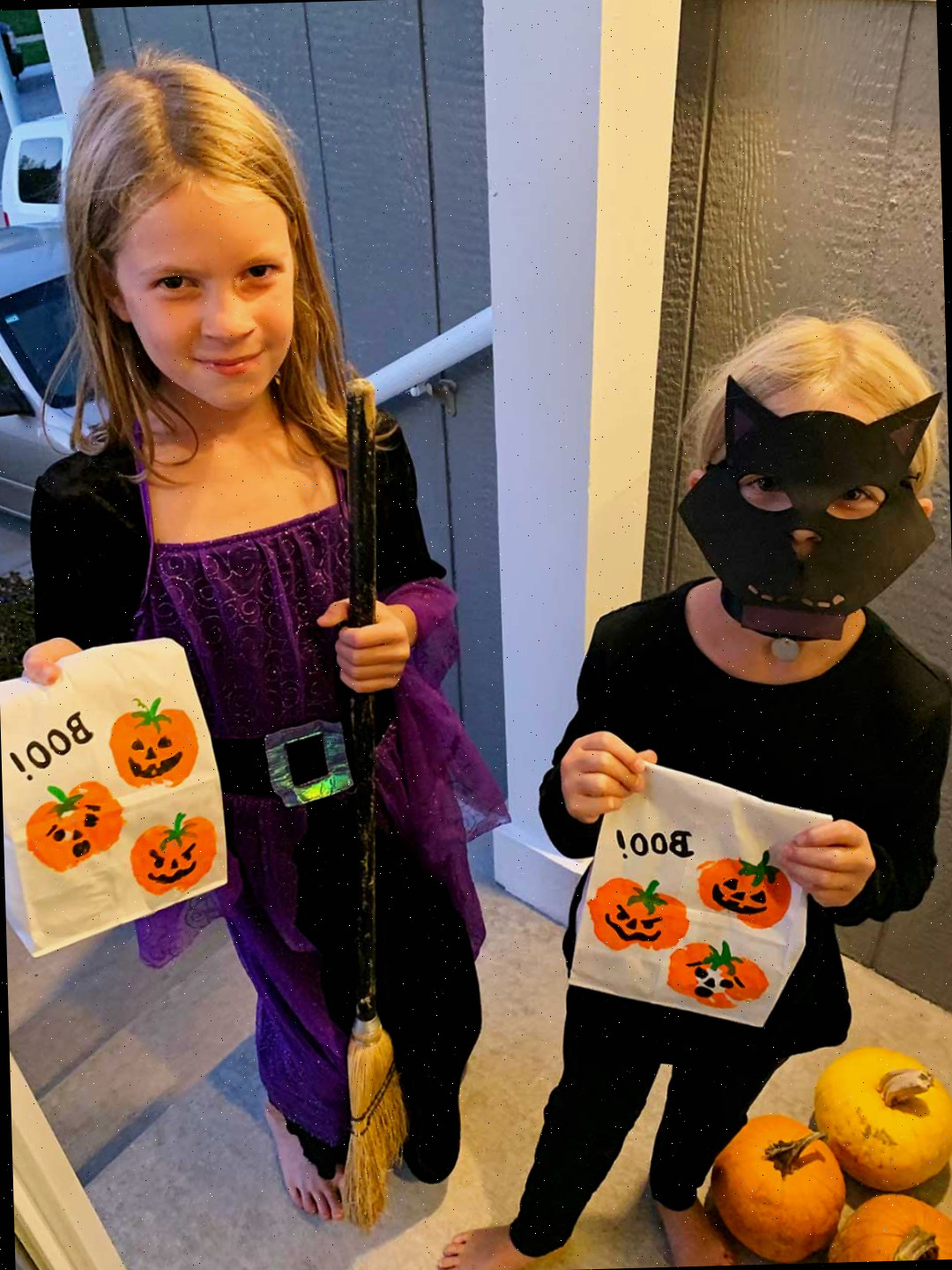 Duas meninas jovens, vestidas de gato preto e bruxa, fazendo trick or treating.