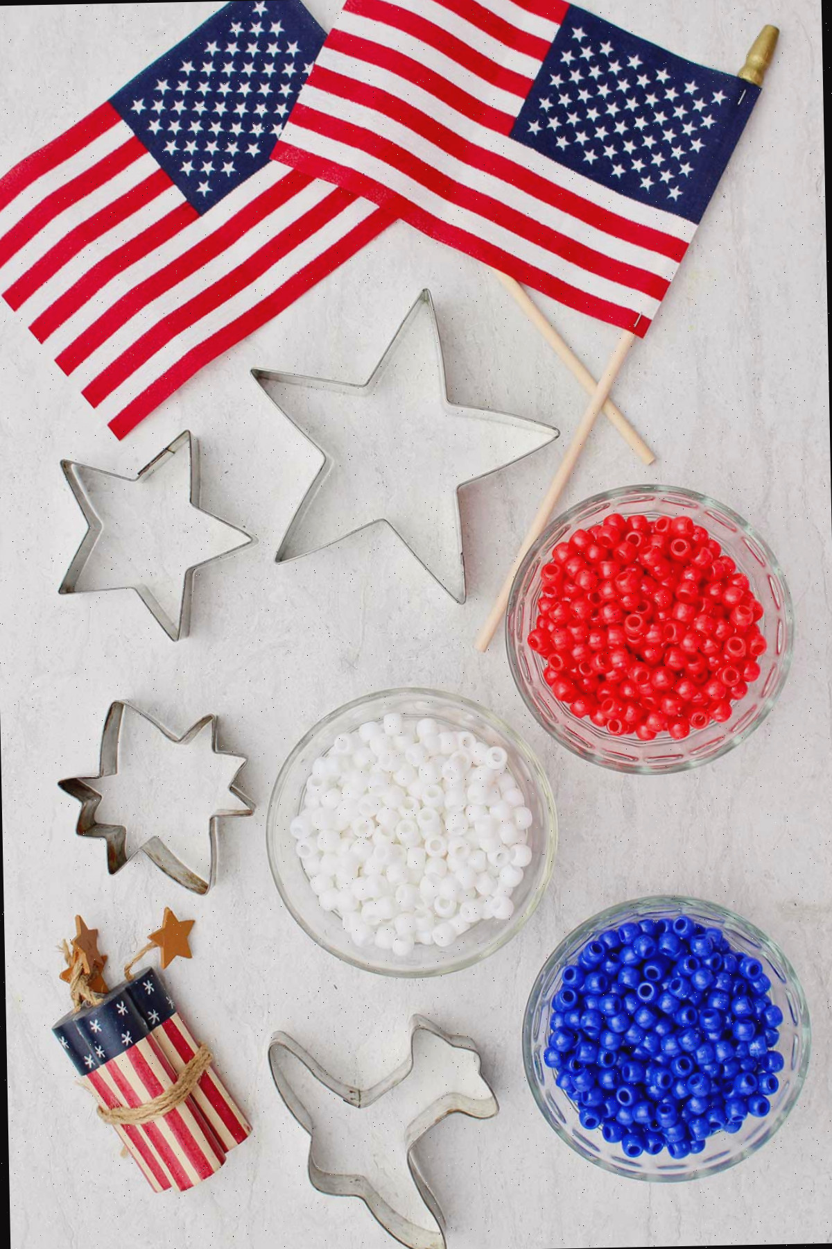 Três tigelas cheias de pérolas vermelhas, brancas e azuis, cortadores de biscoitos e decorações de bandeira americana.