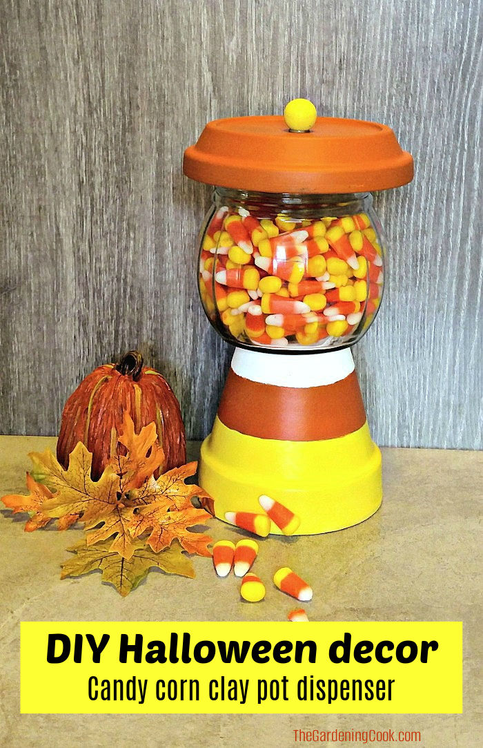 Um vaso de terracota pintado, prato e jarro de vidro transformados em um pote de doces de Halloween. A caixa de texto amarela diz decoração DIY de Halloween - dispensador de pote de barro de doces de milho