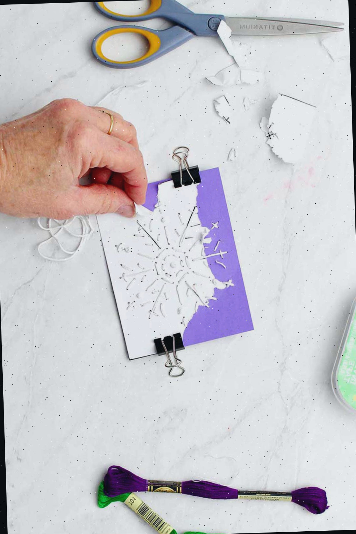 Mão rasgando o modelo de floco de neve de papel branco do cartão roxo.