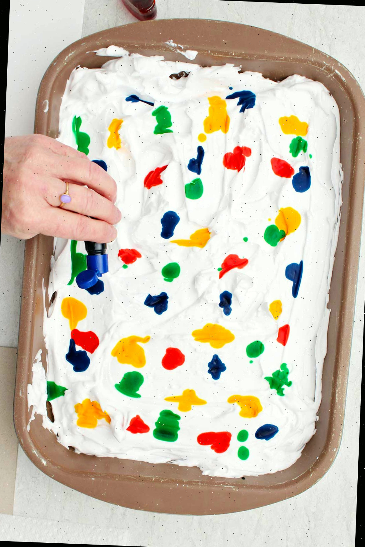 Pessoa borrifando gotas de corante alimentar em uma panela de creme de barbear alisado.