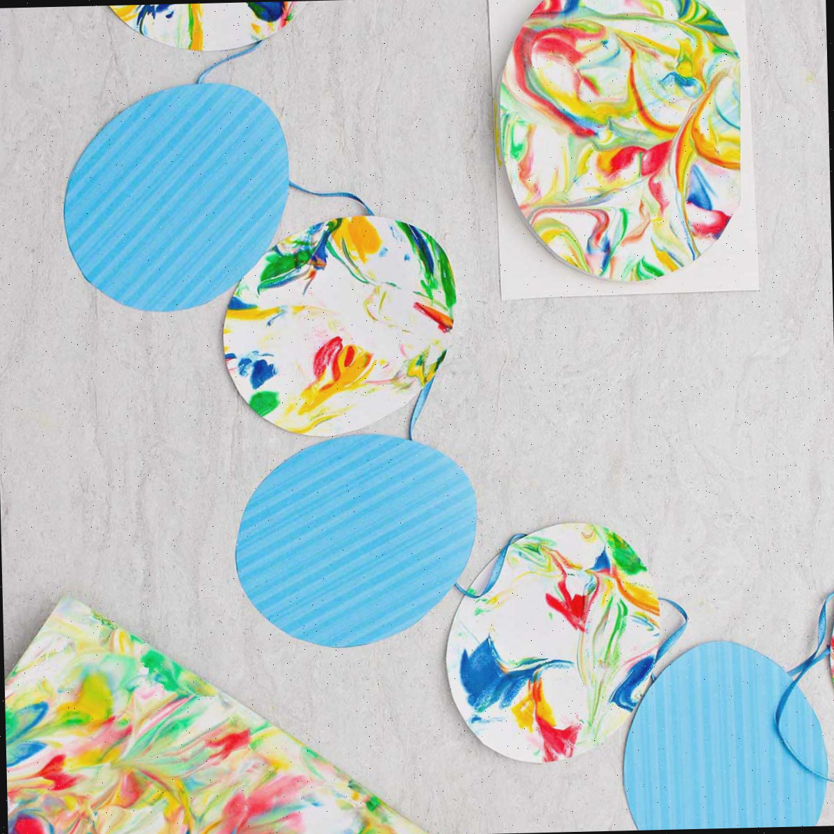 Bandeirinhas de ovo de Páscoa feitas com ovos de papel listrados azuis e ovos de papel marbrado em uma fita azul com outros pedaços de papel marbrado ao redor.