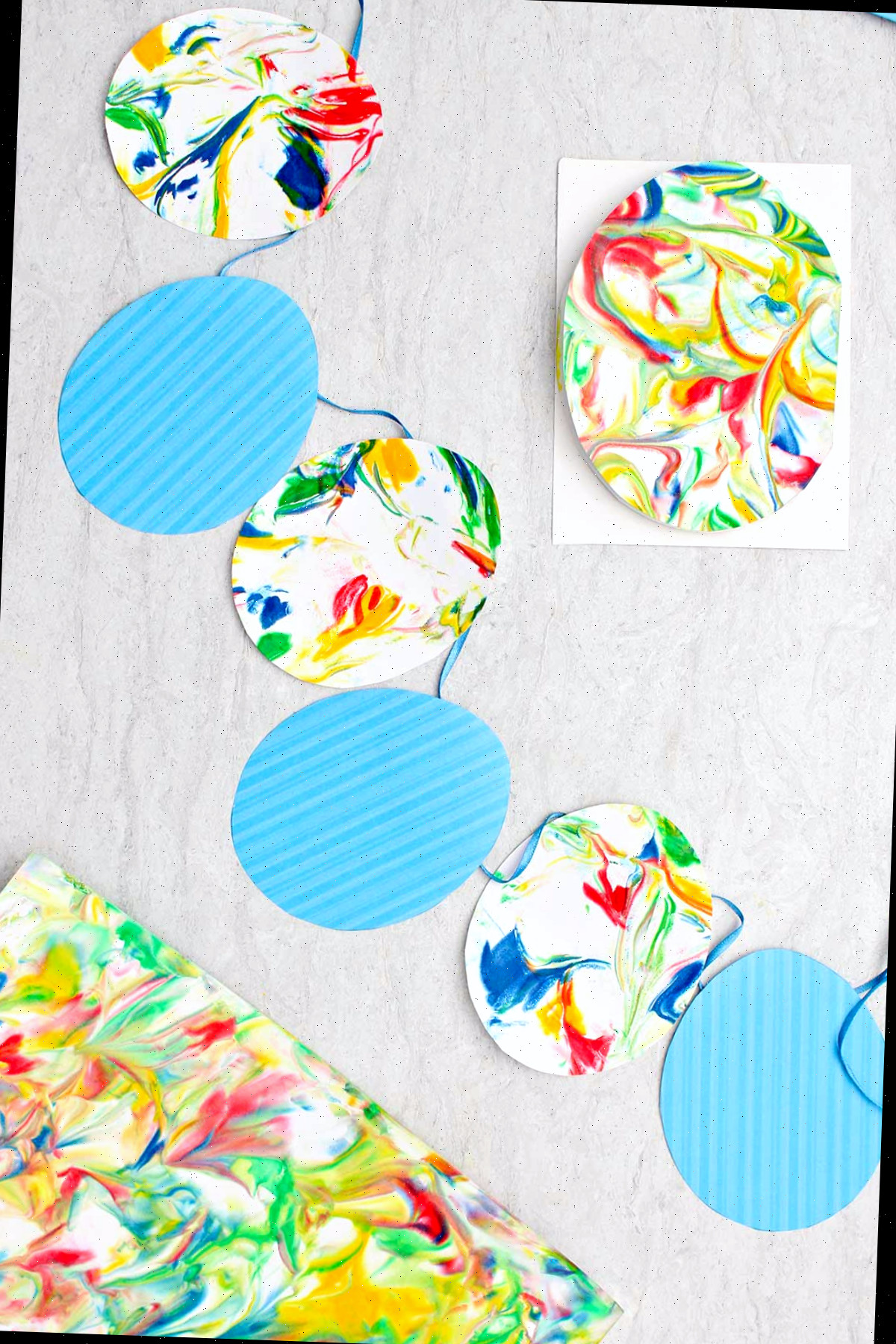 Bandeirinhas de ovo de Páscoa confeccionadas com ovos de papel listrados azuis e ovos de papel marbrado em uma fita azul, rodeados por outras peças de papel marbrado.