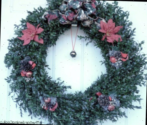 Guirlanda de Natal Buxo com sino e decorações em uma porta branca.