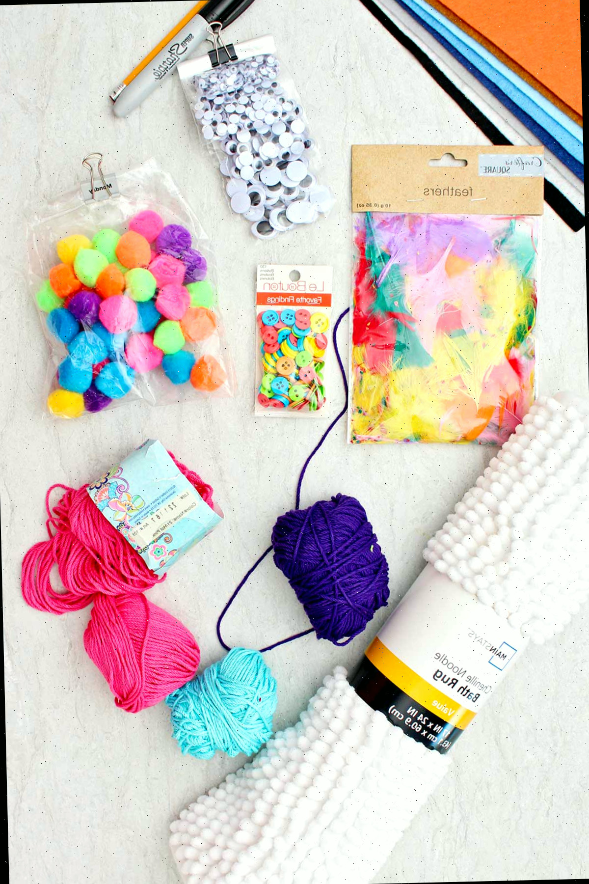 Itens para confeccionar fantasias de Halloween DIY. Olhos de insetos, penas, pompons, cordão colorido, botões e um tapete de banho branco.