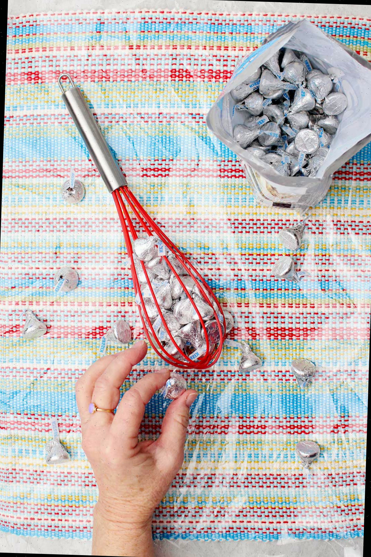 Indivíduo colocando Hershey Kisses dentro de um batedor de silicone vermelho.