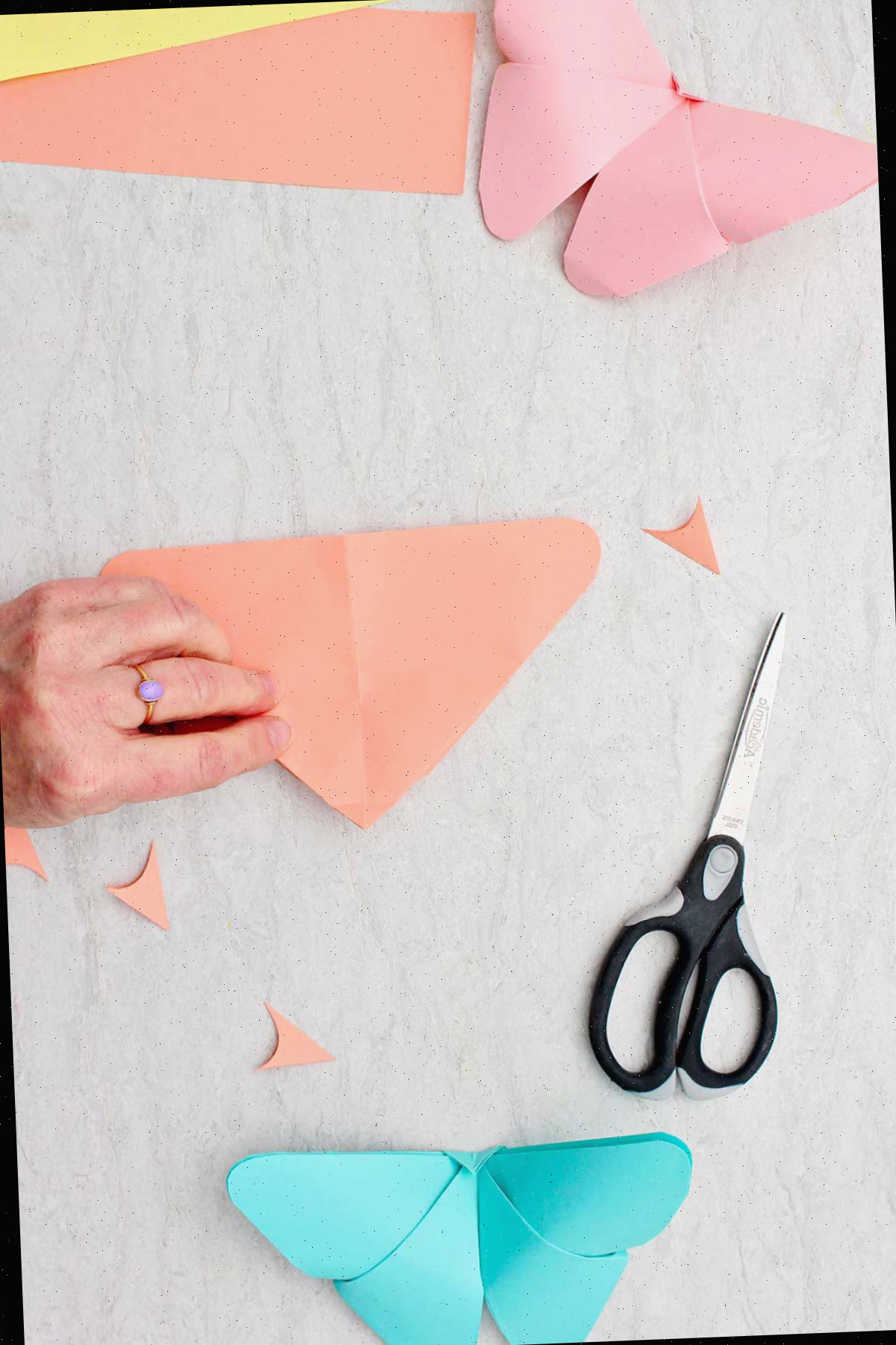 Uma pessoa dobrando uma folha de papel laranja na forma de um triângulo com o ponto superior voltado para baixo.