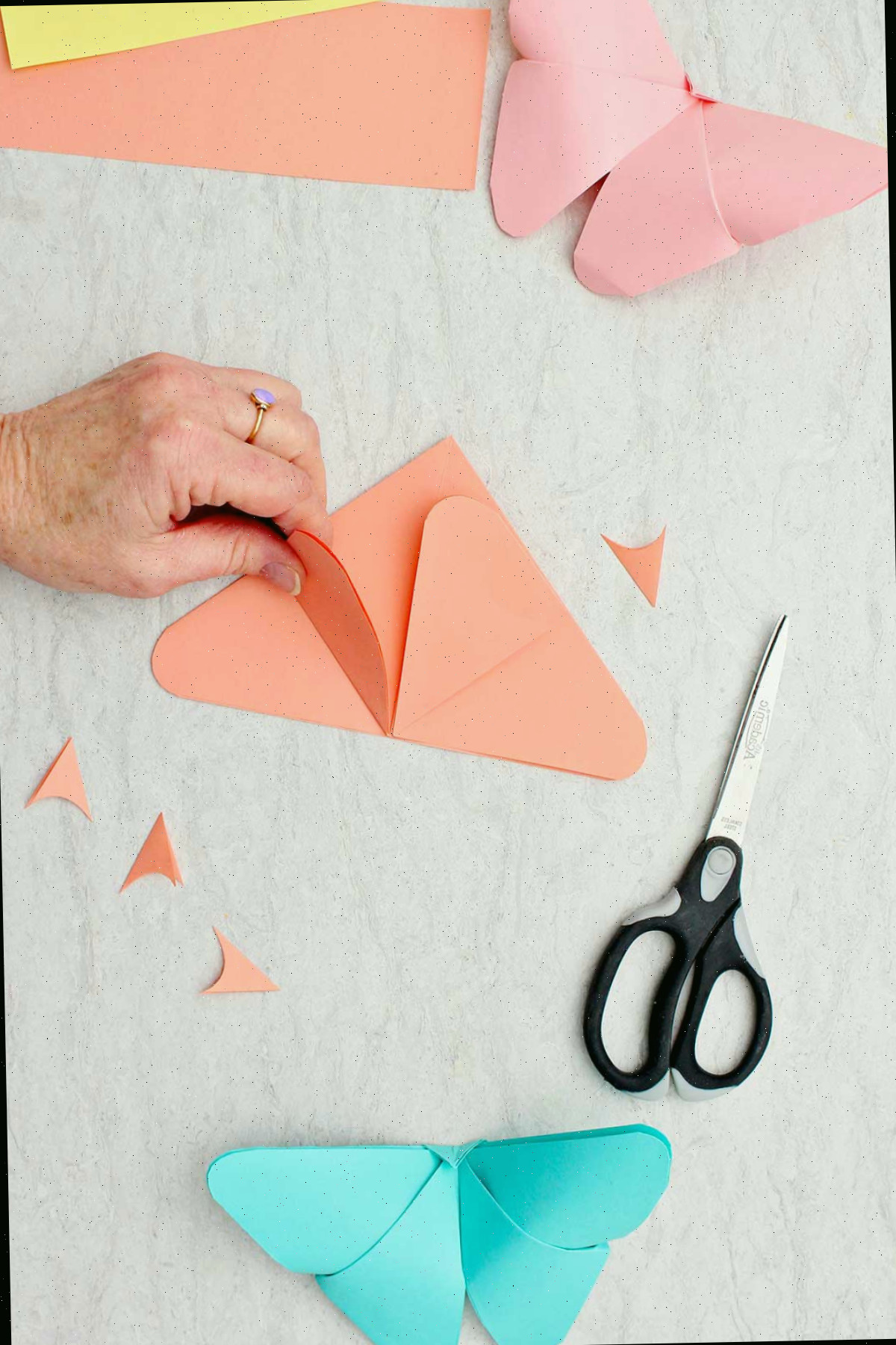 Uma pessoa elevando as bordas arredondadas em um pedaço de papel laranja dobrado em triângulo.