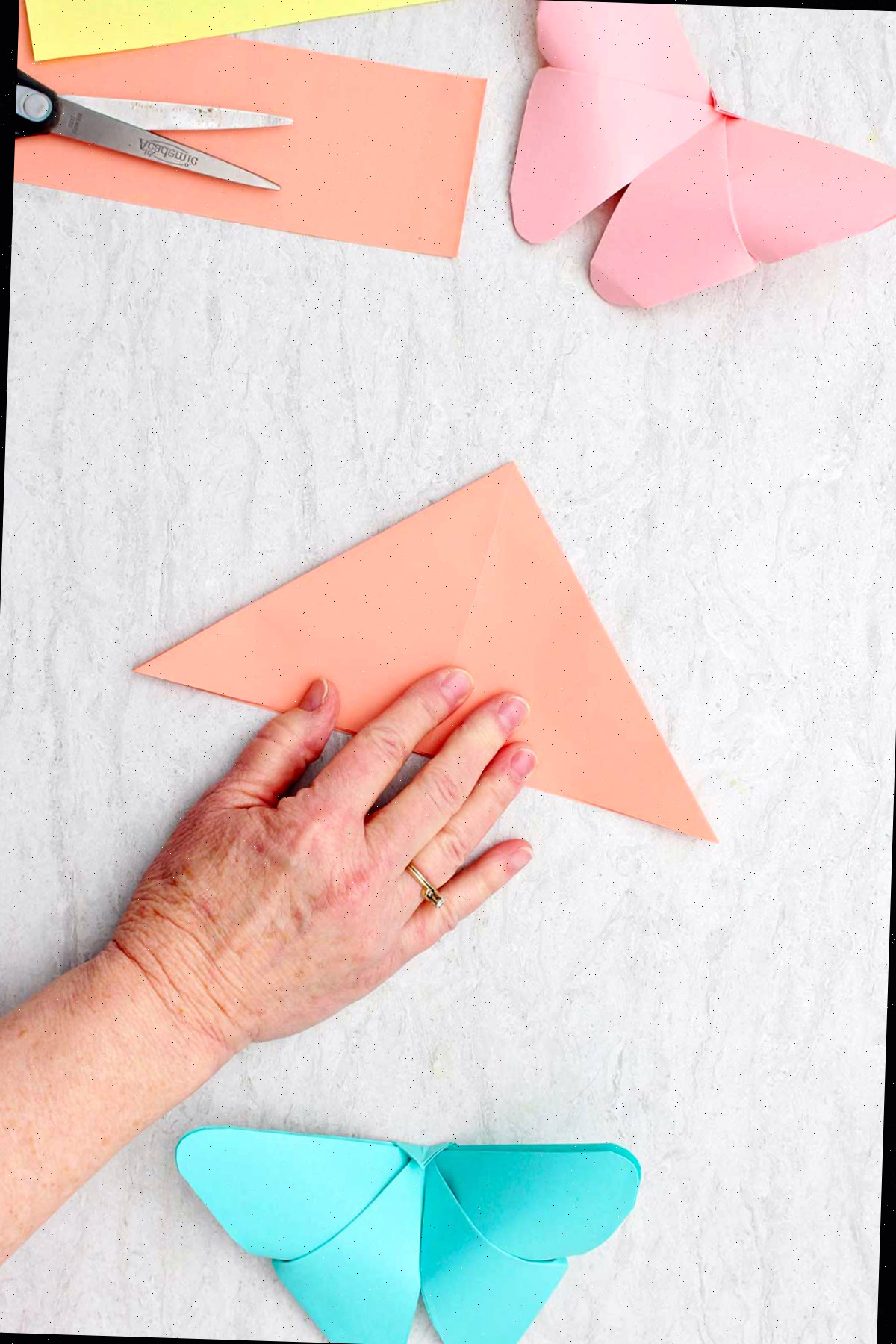 Uma pessoa dobrando uma folha de papel laranja na forma de um triângulo menor.
