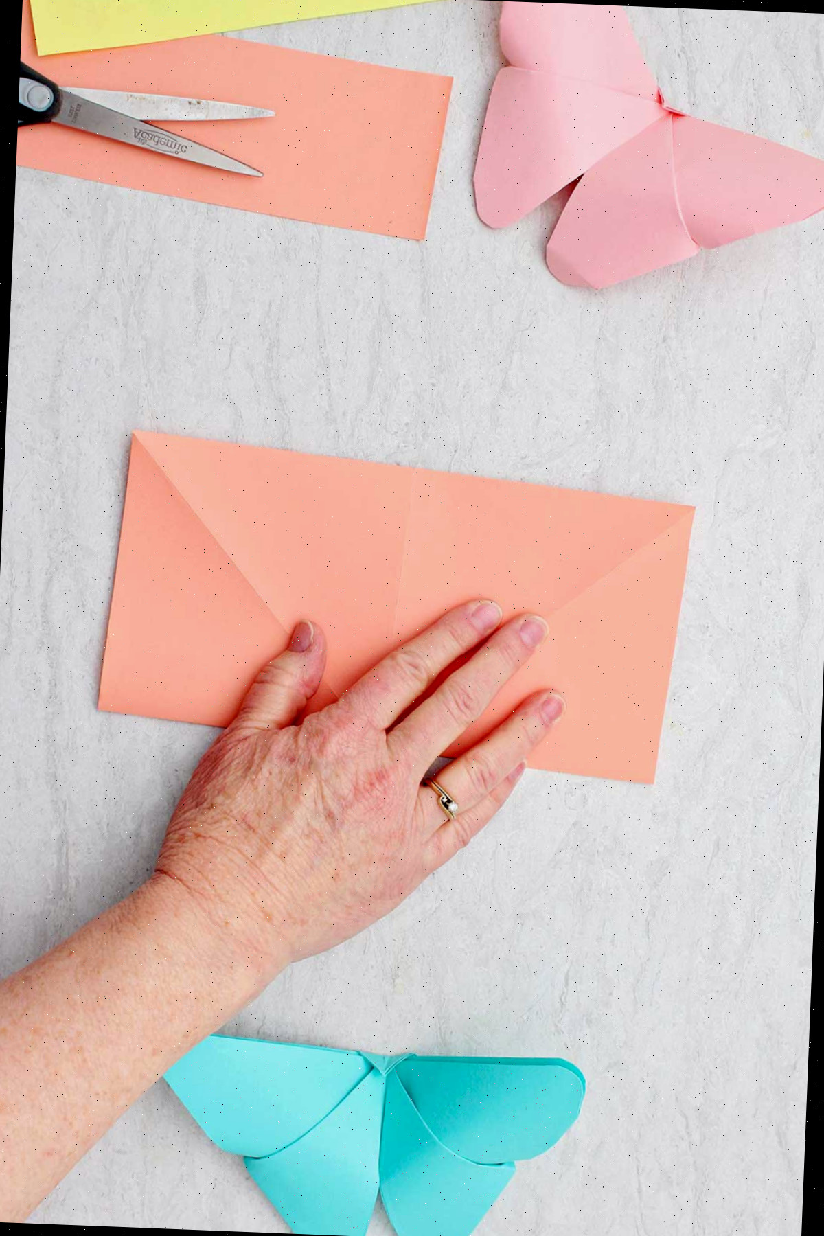 Uma pessoa dobrando uma folha de papel laranja na forma de um retângulo.