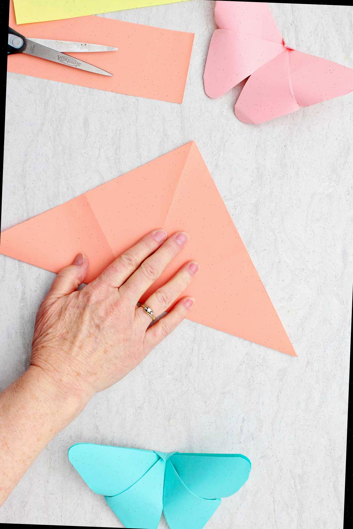 Uma pessoa dobrando uma folha de papel laranja na forma de um triângulo.