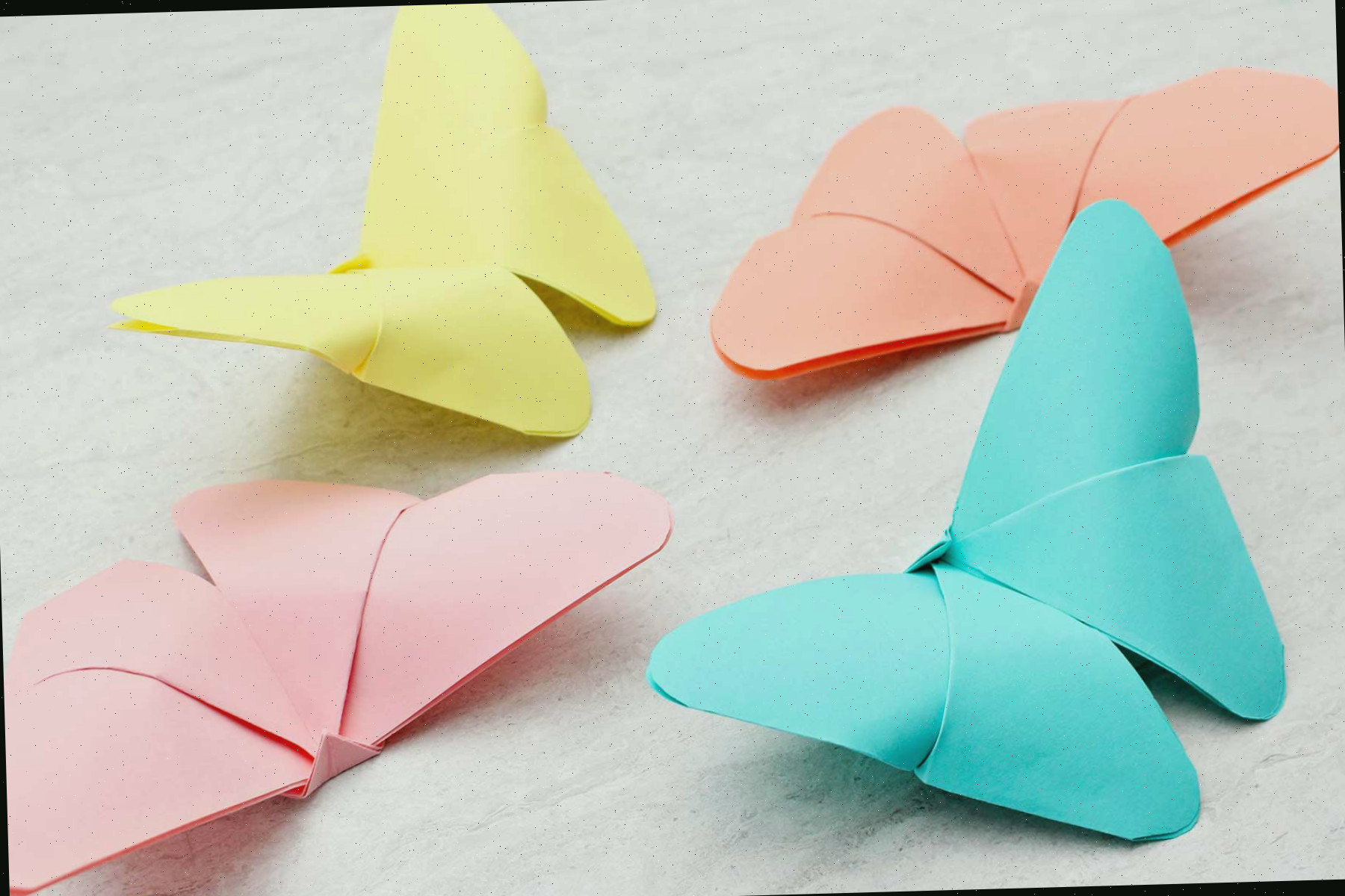 Quatro borboletas de origami em tonalidades pastel de azul, amarelo, laranja e rosa.
