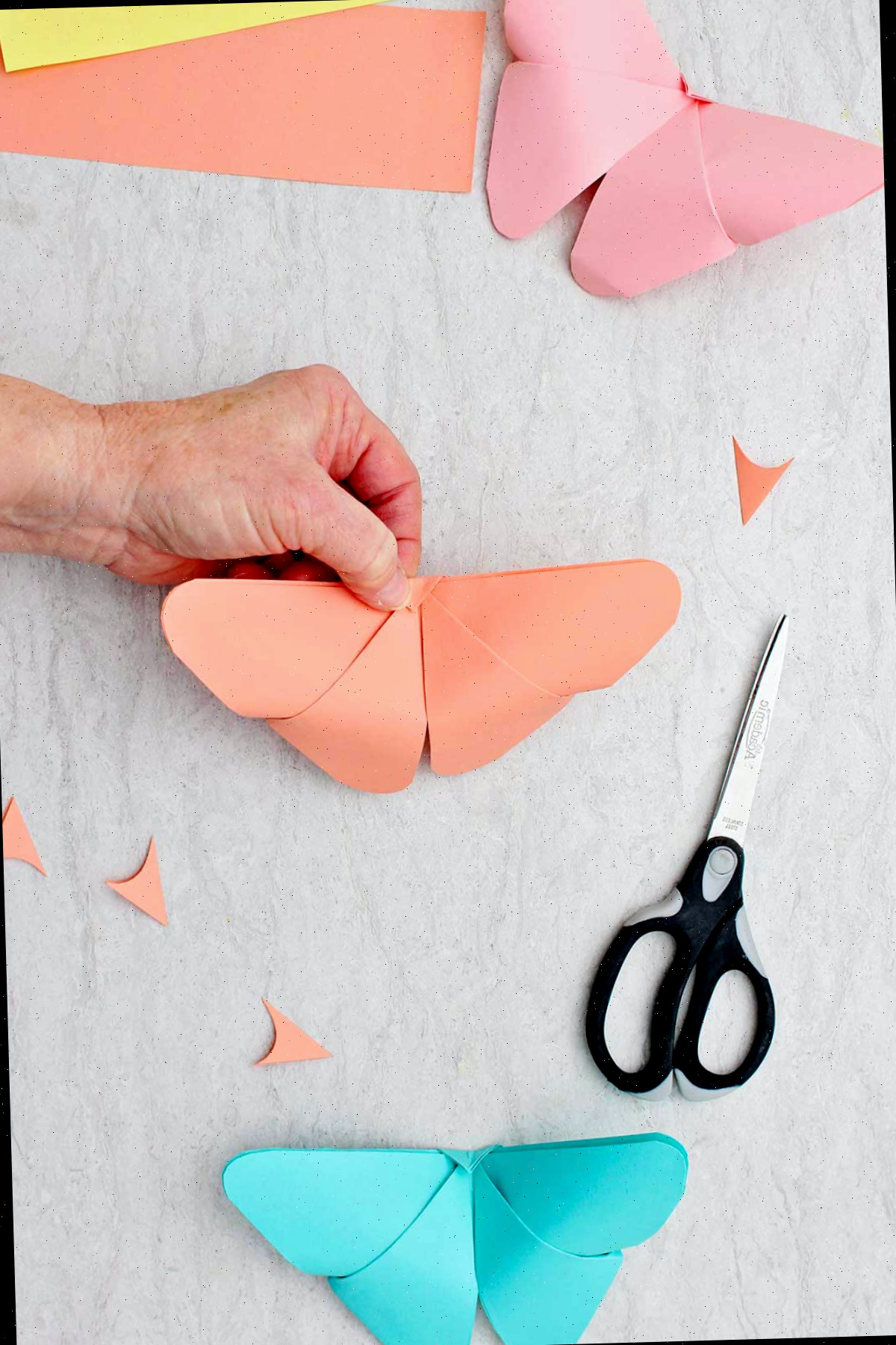 Uma pessoa mostrando o outro lado da ponta do triângulo dobrado em uma borboleta de origami finalizada.
