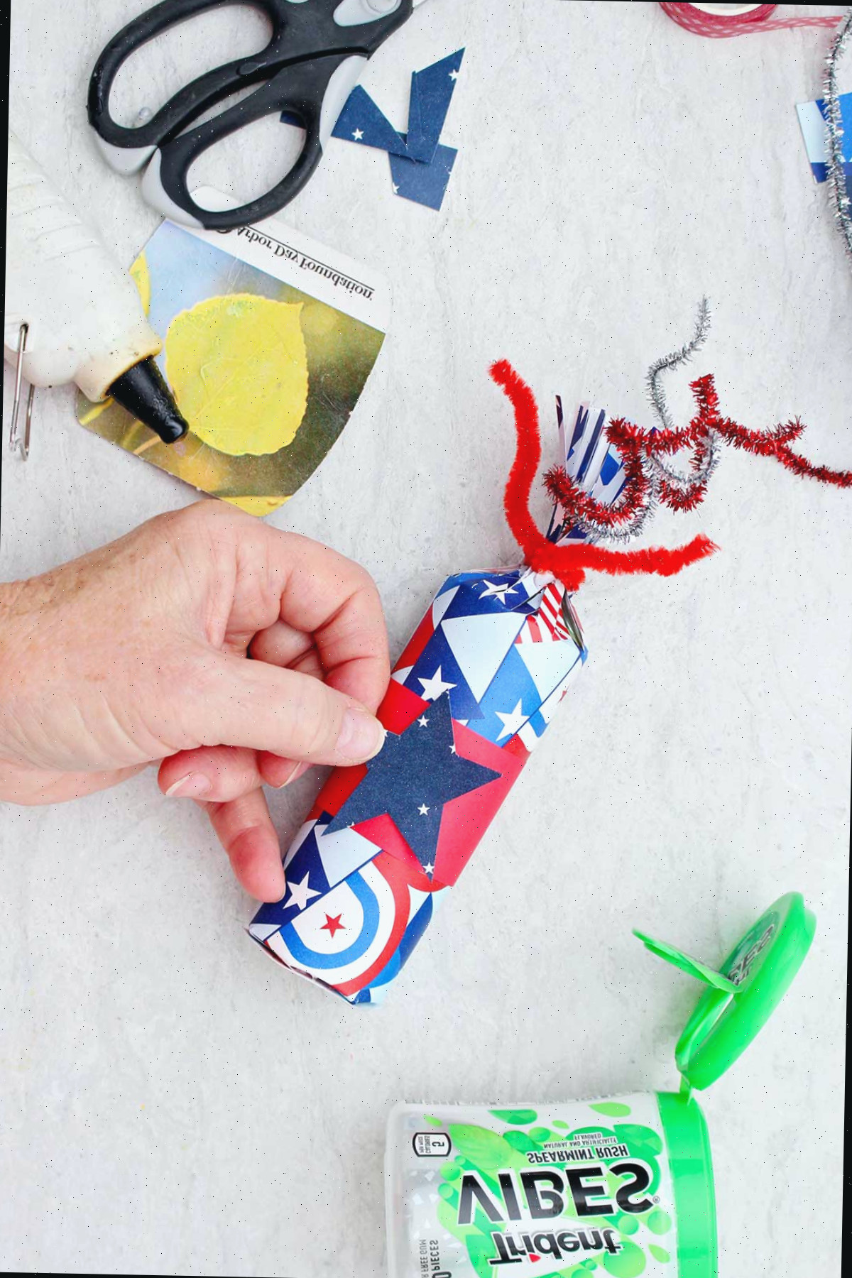 Pessoa colocando um pedaço de papel de scrapbook azul em forma de estrela em uma caixa de guloseima finalizada do 4 de Julho.