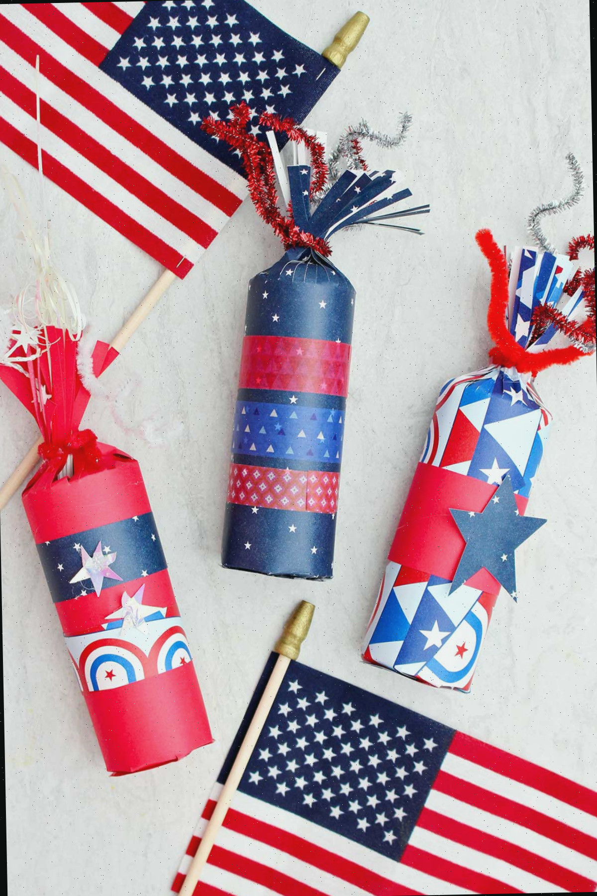 Três caixas de guloseimas em forma de fogos de artifício decoradas com papéis vermelhos, brancos e azuis e fita washi, com duas pequenas bandeiras americanas como decoração.