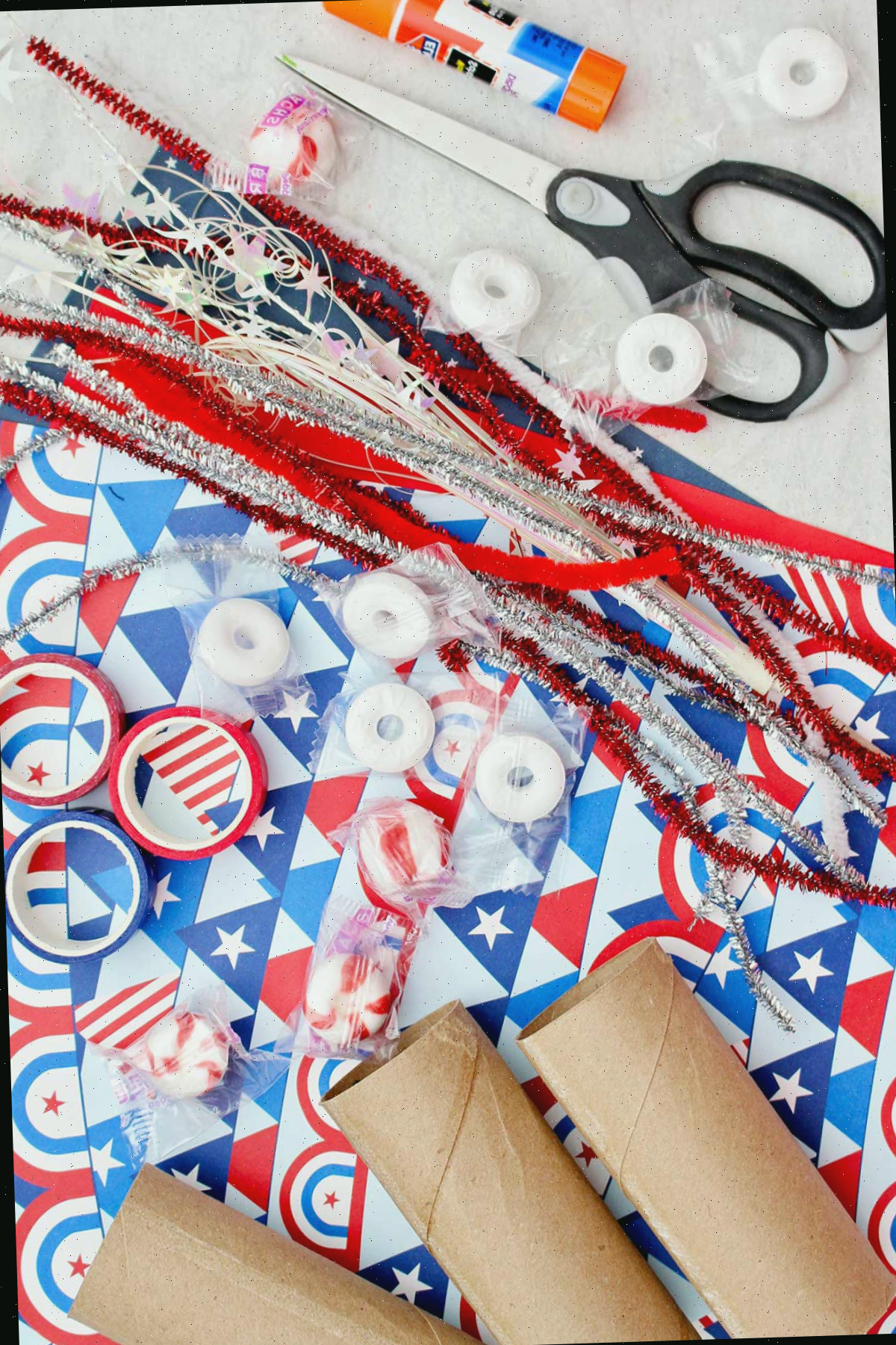 Fitas de limpador de cachimbo brilhantes, papel de scrapbook vermelho, branco e azul, fita washi vermelha e azul, rolos de papel toalha, tesoura, cola e balas para colocar nas caixas de doces.