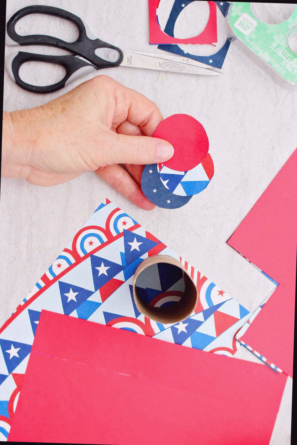Pessoa segurando três recortes circulares de papel de scrapbook que serão usados para fechar a extremidade inferior de uma caixa de guloseimas em forma de foguete.