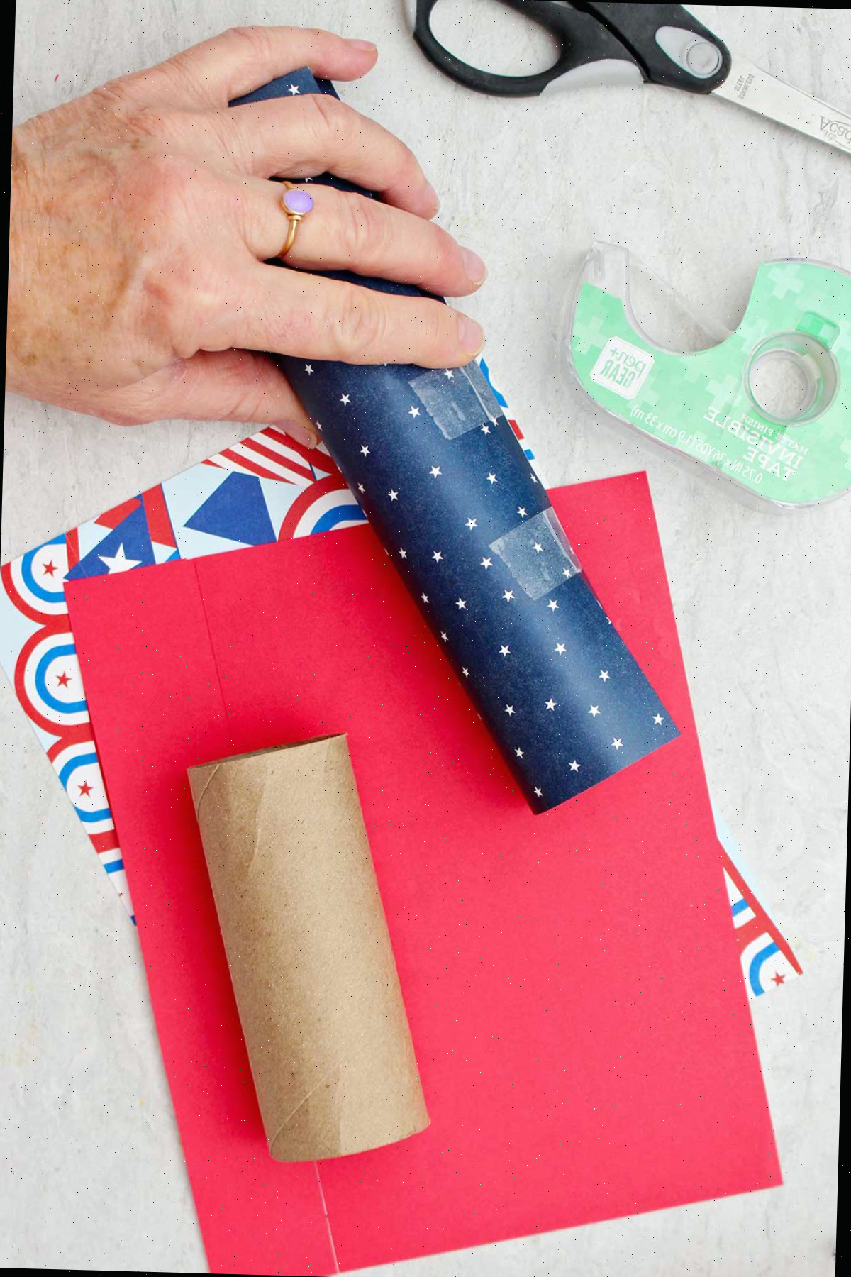 Pessoa segurando um tubo de papel higiênico envolto em papel de scrapbook com padrão de estrelas azuis e colado.