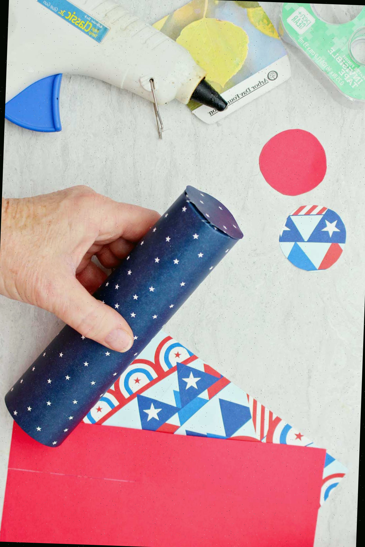 Indivíduo demonstrando como fixar um pedaço circular de papel de scrapbook na parte inferior do tubo de papel higiênico para selar a extremidade.