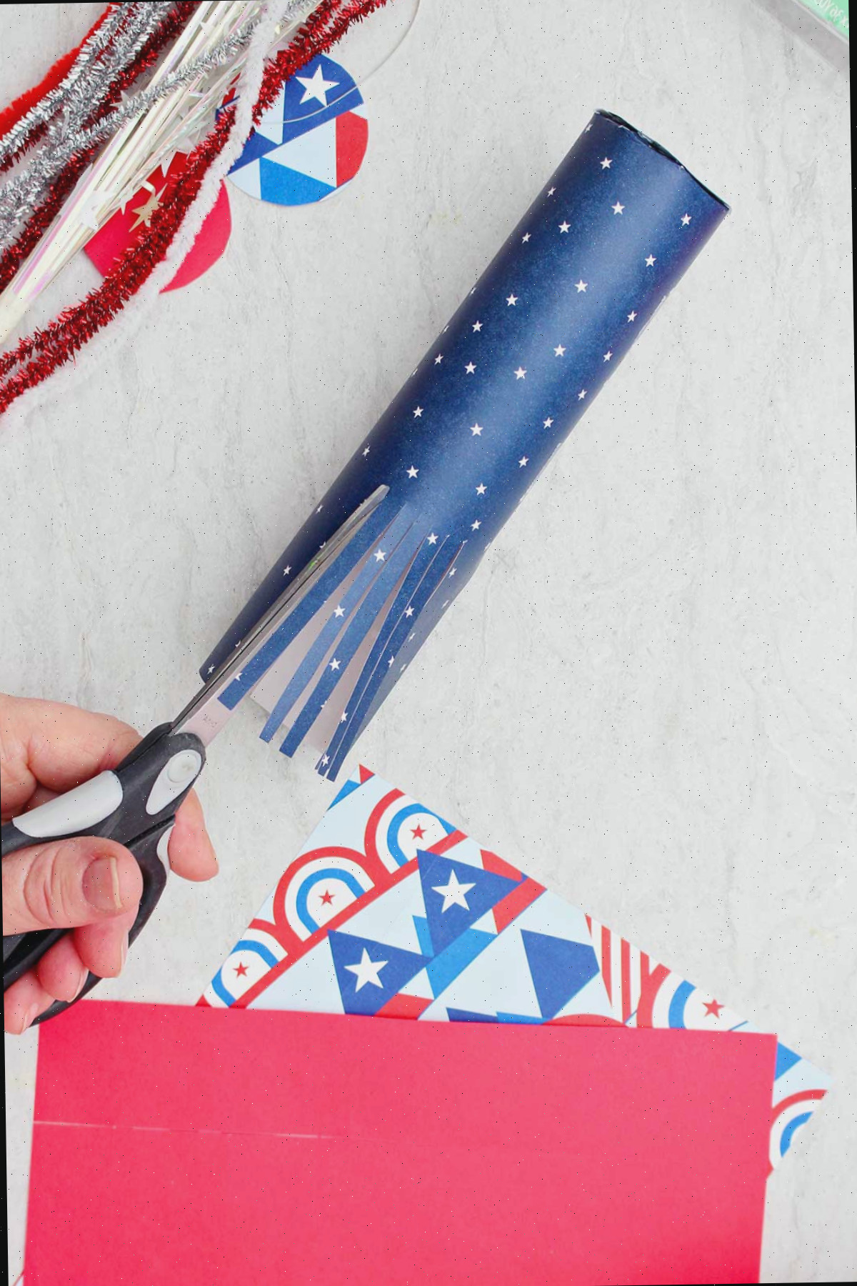 Indivíduo cortando papel de scrapbook enrolado em um tubo de papel higiênico para criar aparência de franjas.
