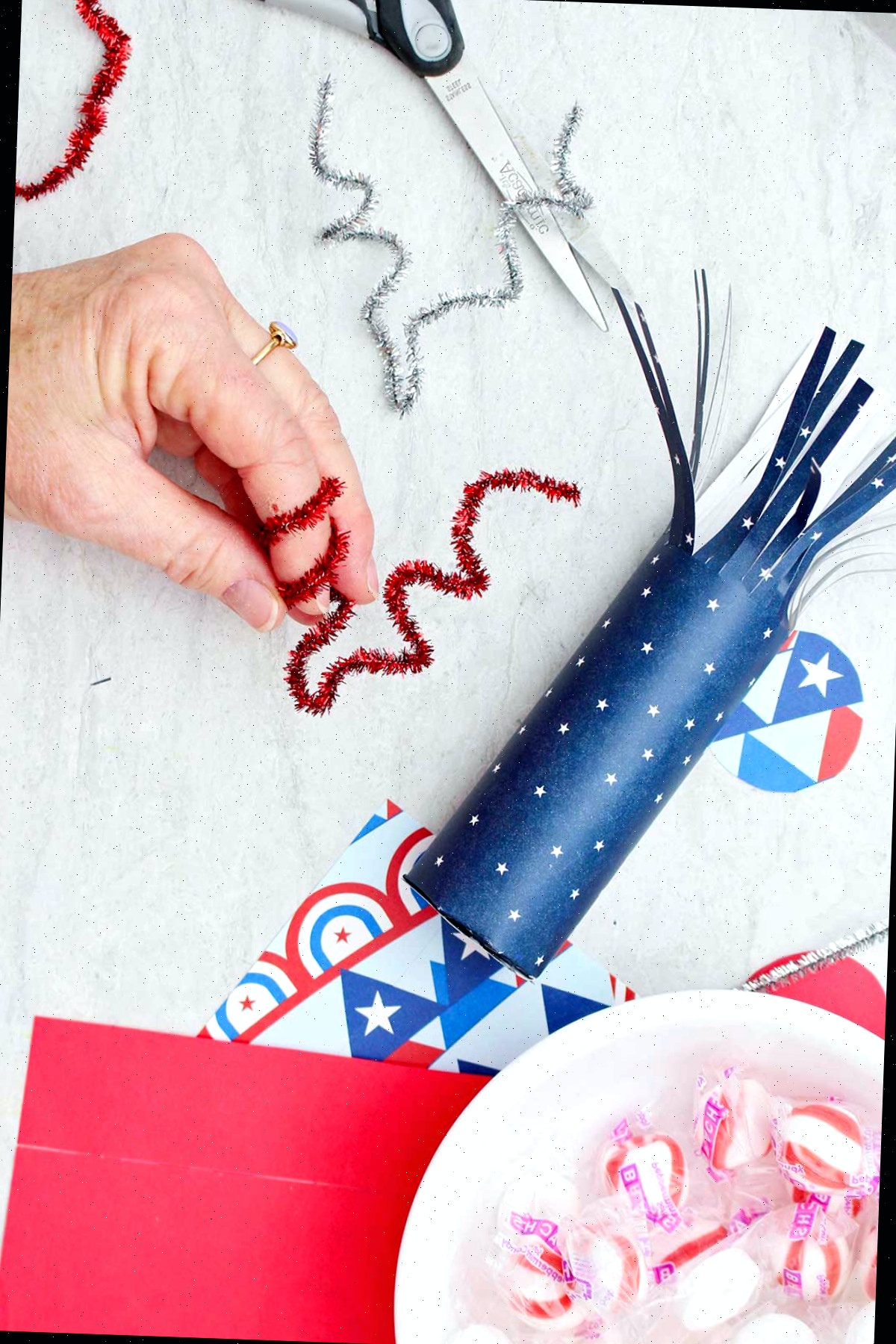 Indivíduo torcendo um limpa-pipas vermelho brilhante ao redor do dedo para dar-lhe uma forma torcida.