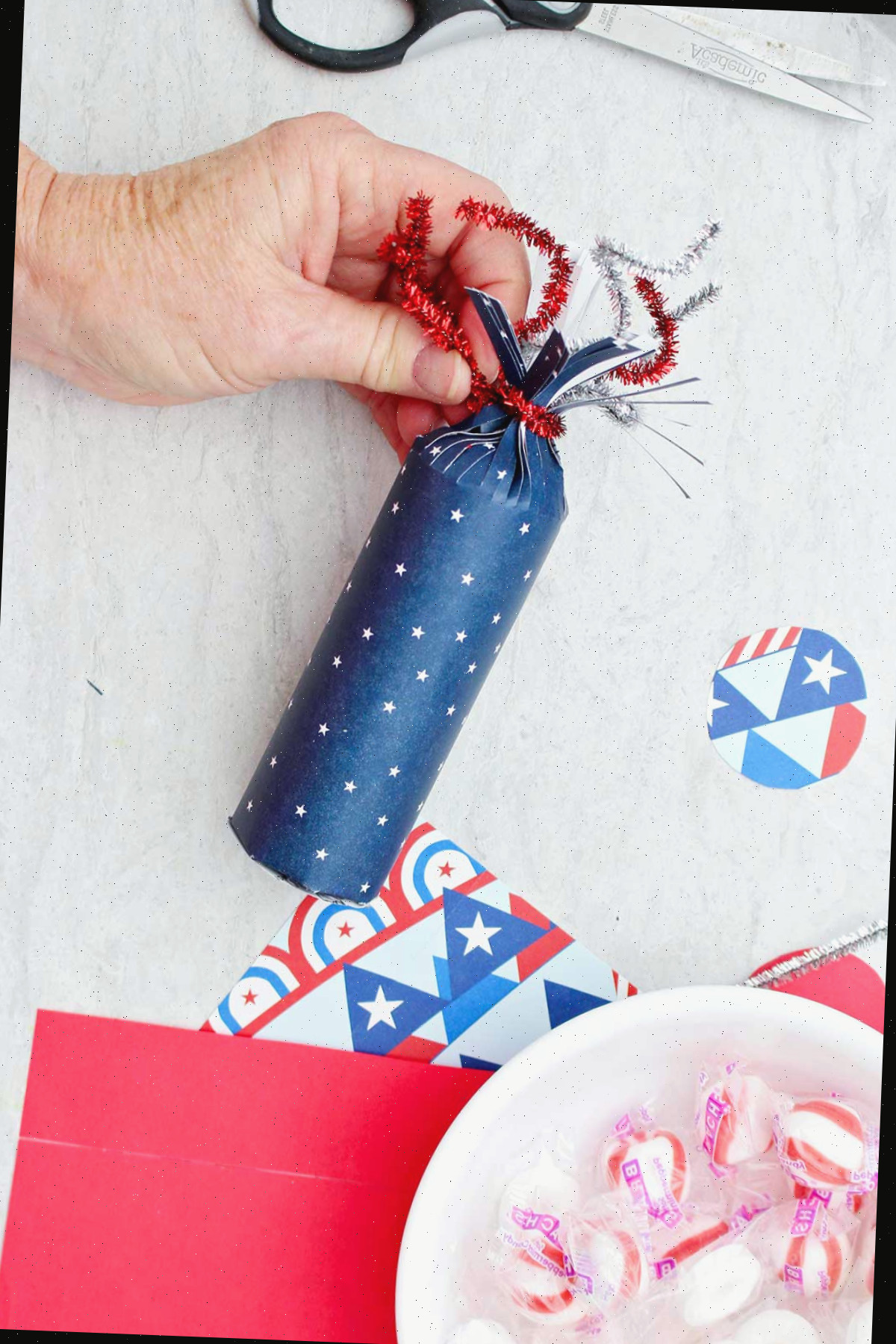 Indivíduo enrolando um limpador de pipas vermelho brilhante no topo da caixa de doces em forma de foguete com padrão de estrela azul.