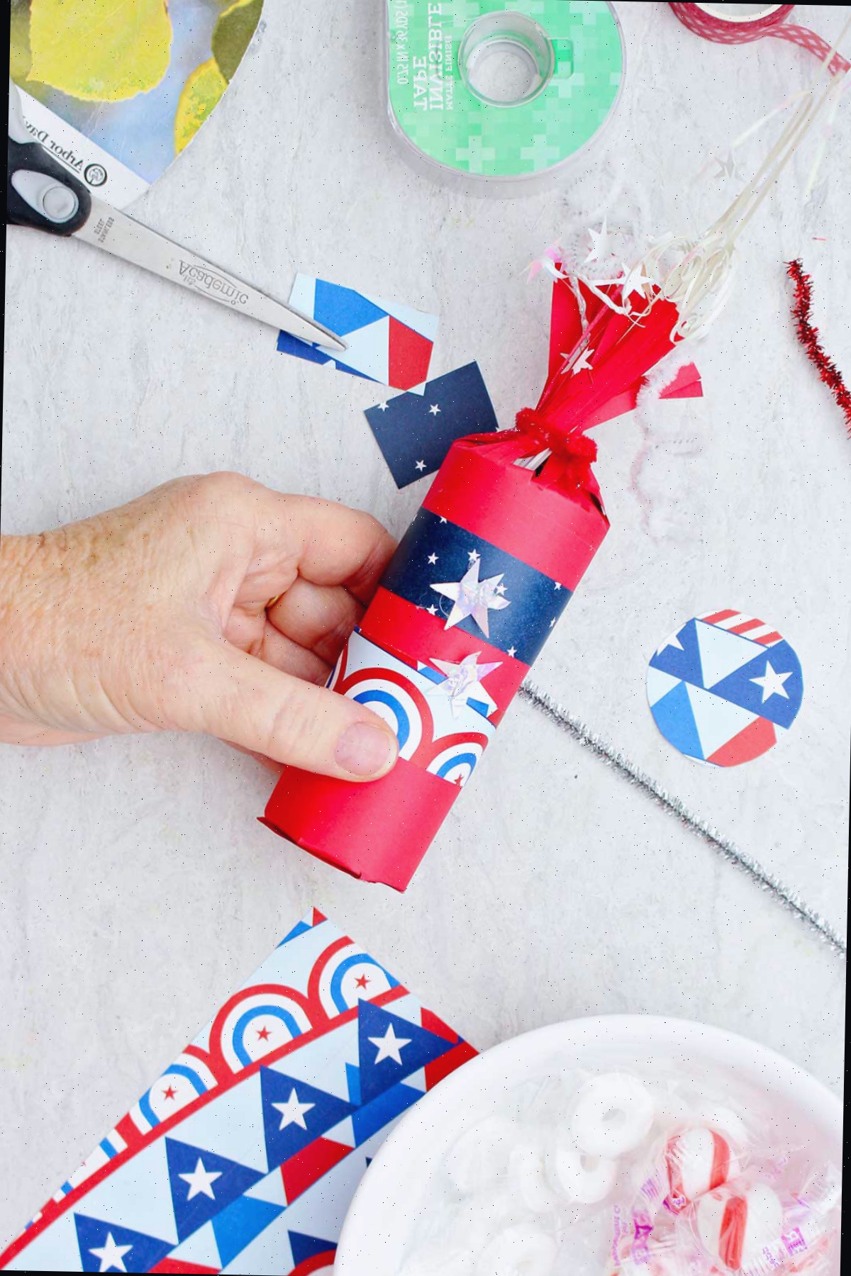 Indivíduo decorando a caixa de doces em forma de foguete vermelha com papel de scrapbook estampado.