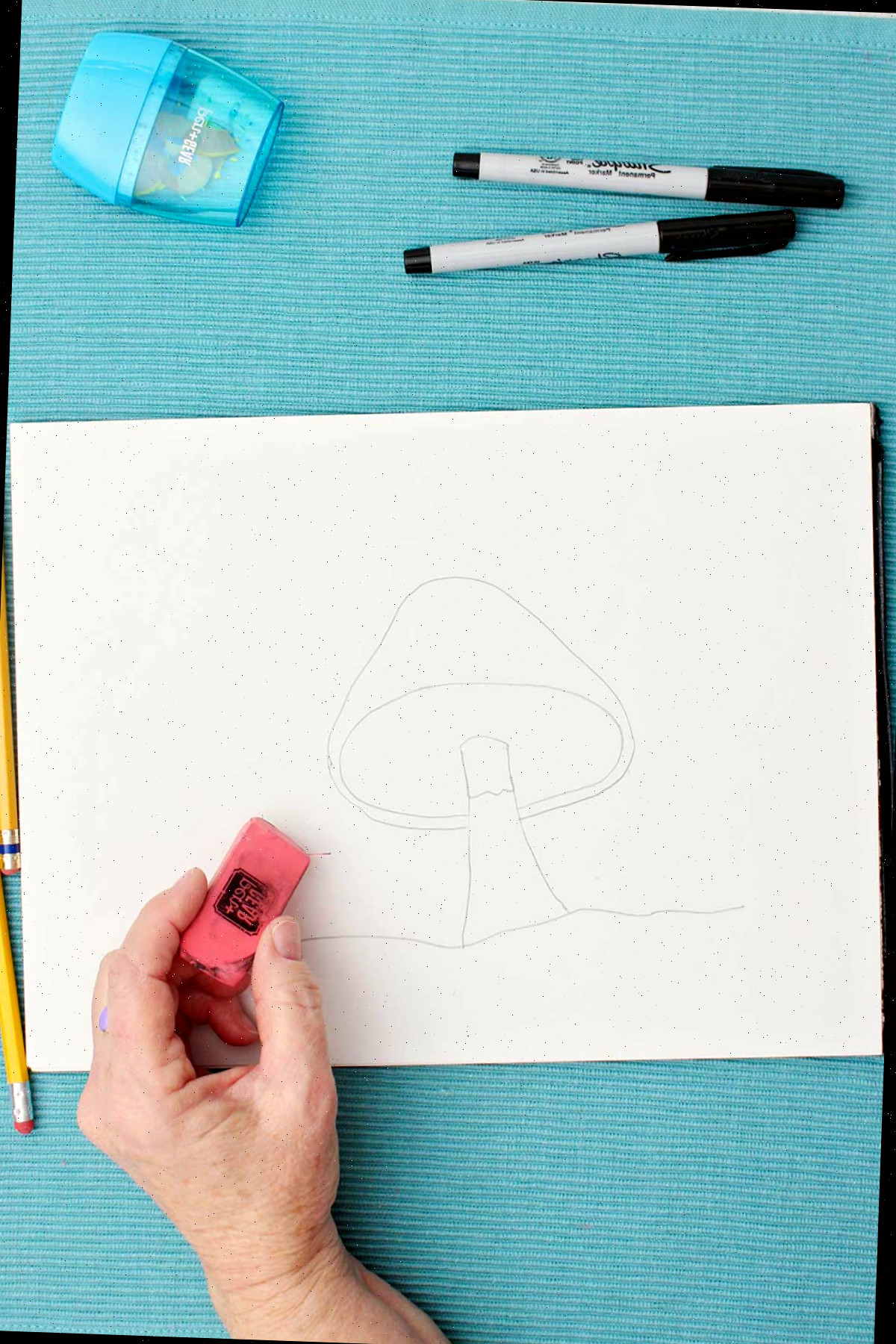 Um artista apagando linhas de um desenho de cogumelo em um pedaço de papel