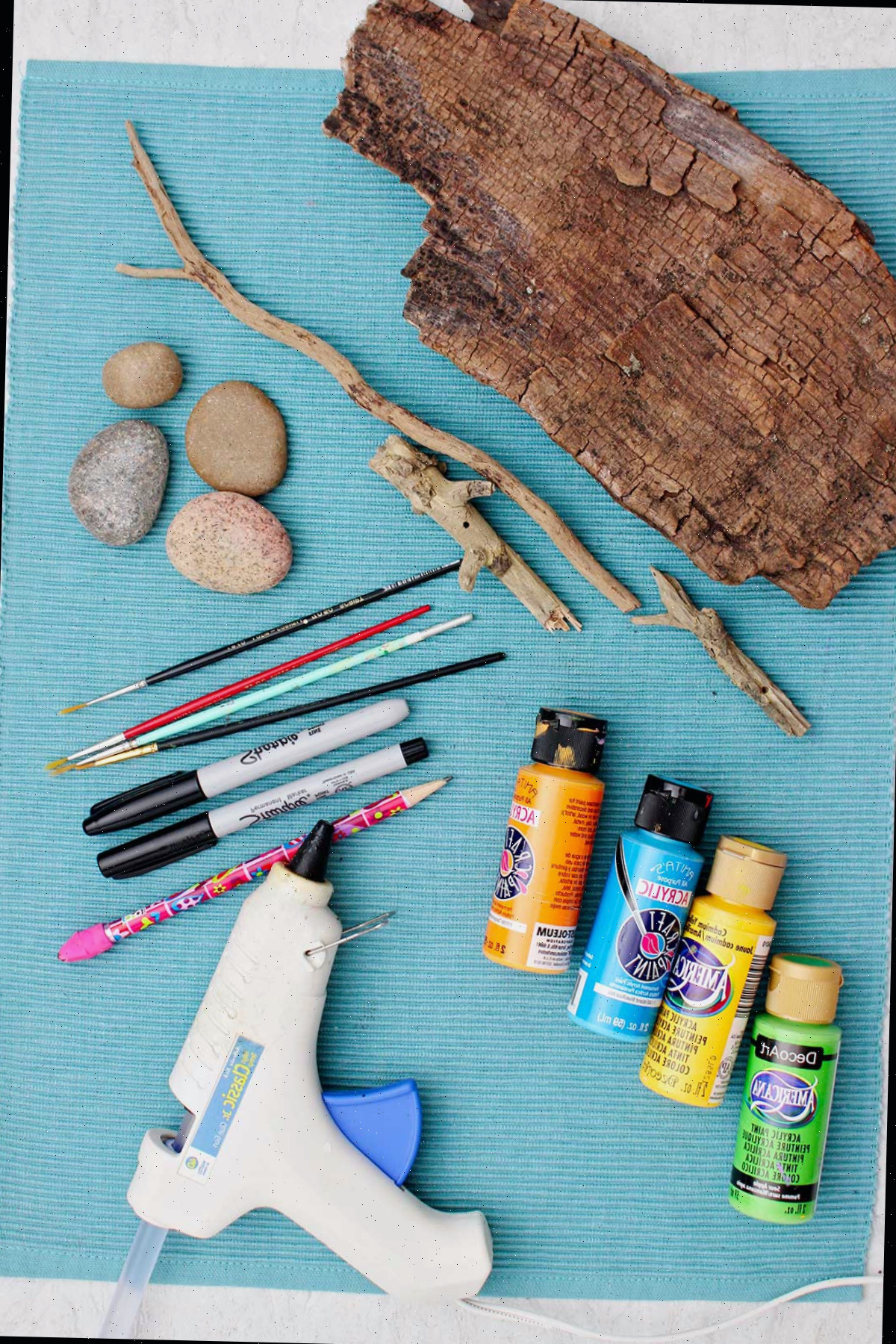Pedras lisas, pincéis, marcadores sharpie, tinta, pistola de cola e pedaços de madeira para fazer arte em pedras pintadas de coruja.