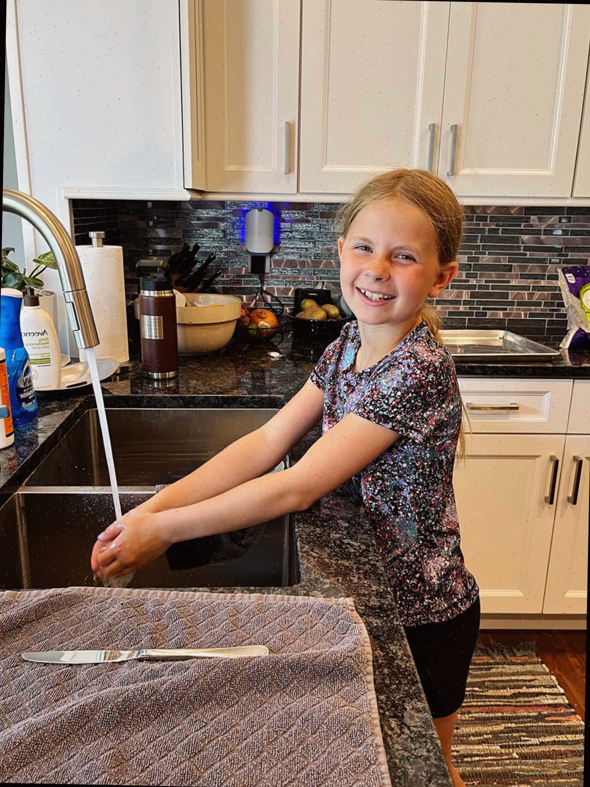 Uma menina com cabelo loiro lavando as mãos na pia da cozinha.