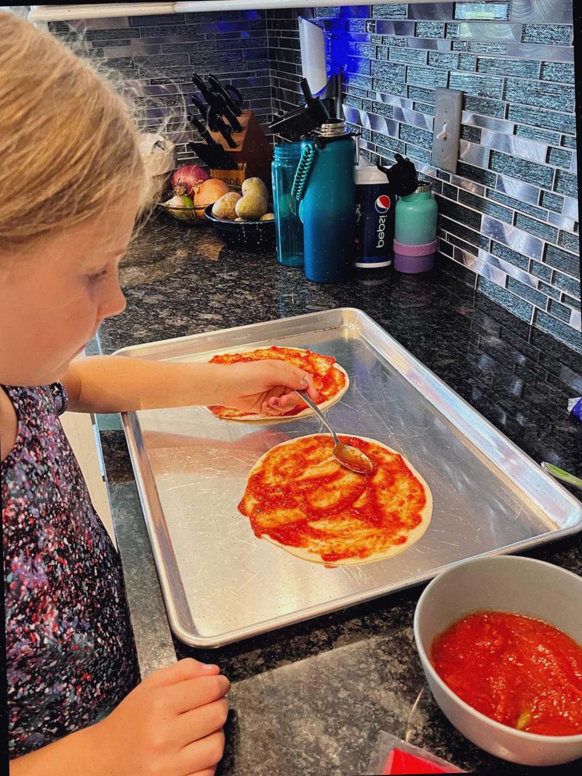 Uma criança aplicando molho na quesadilla de pizza.