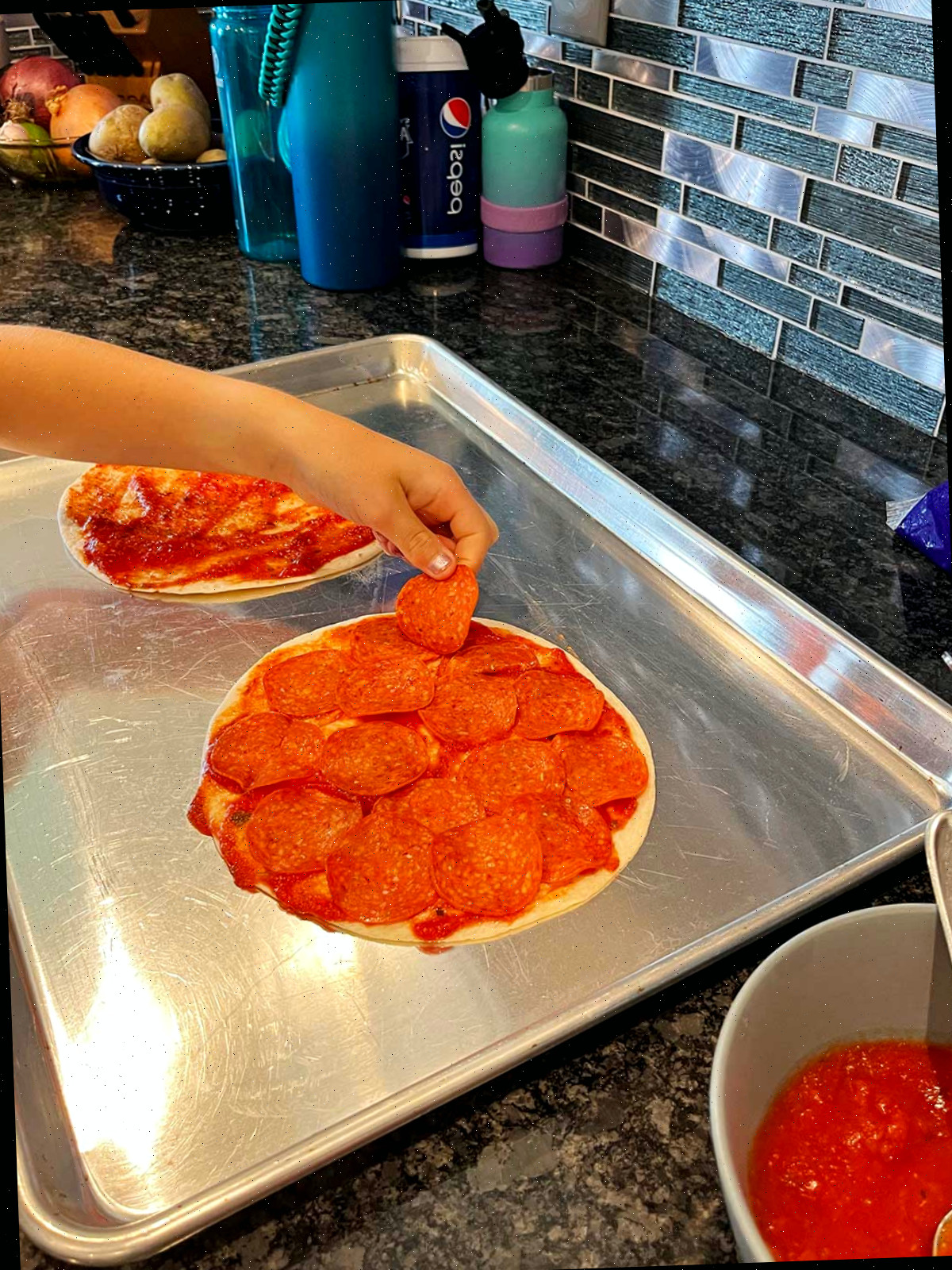 Uma criança adicionando pepperoni na quesadilla de pizza.
