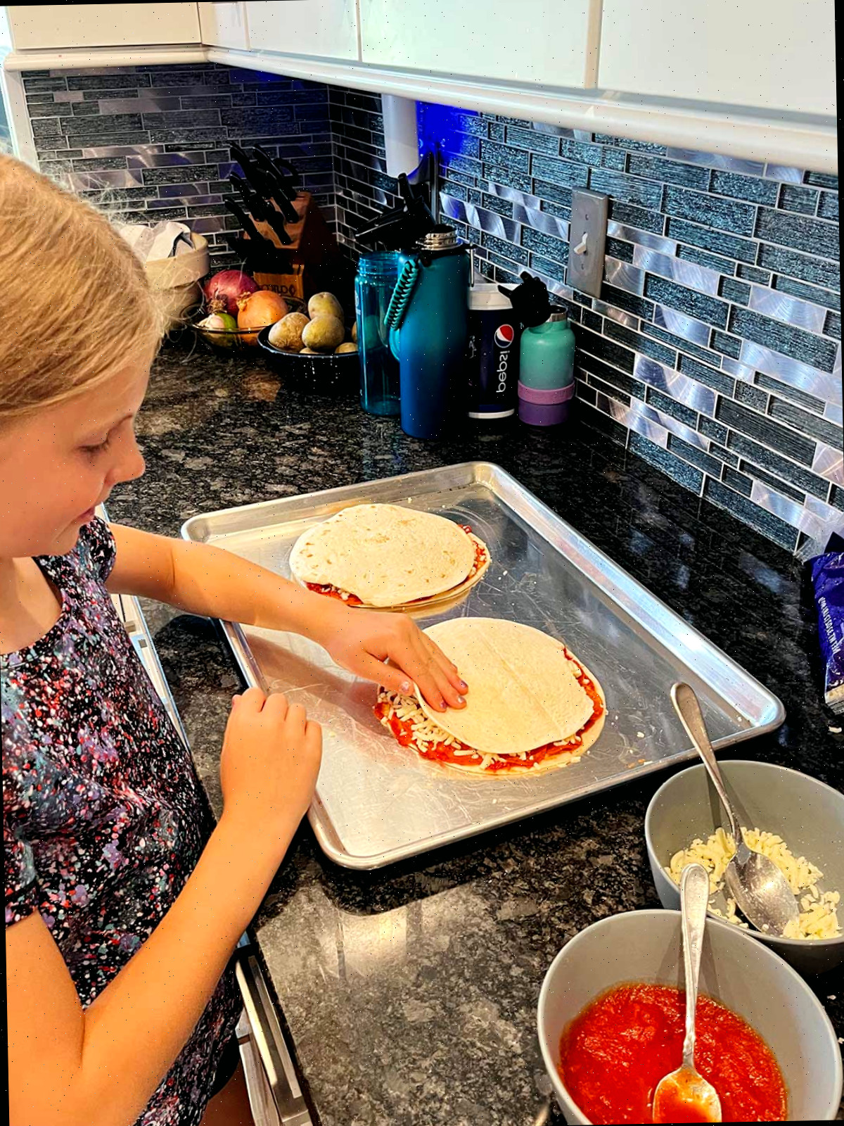 Uma menina jovem montando duas quesadillas de pizza na bancada.