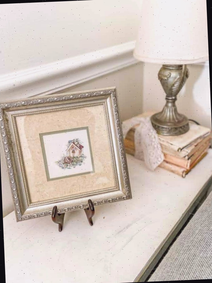 quadro emoldurado de uma casa sobre mesa lateral com livros pintados Um espelho sobre uma mesa