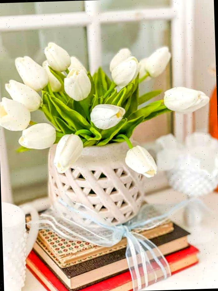 tulipas de seda branca empilhadas sobre livros amarrados com uma fita Um vaso de flores sobre uma mesa