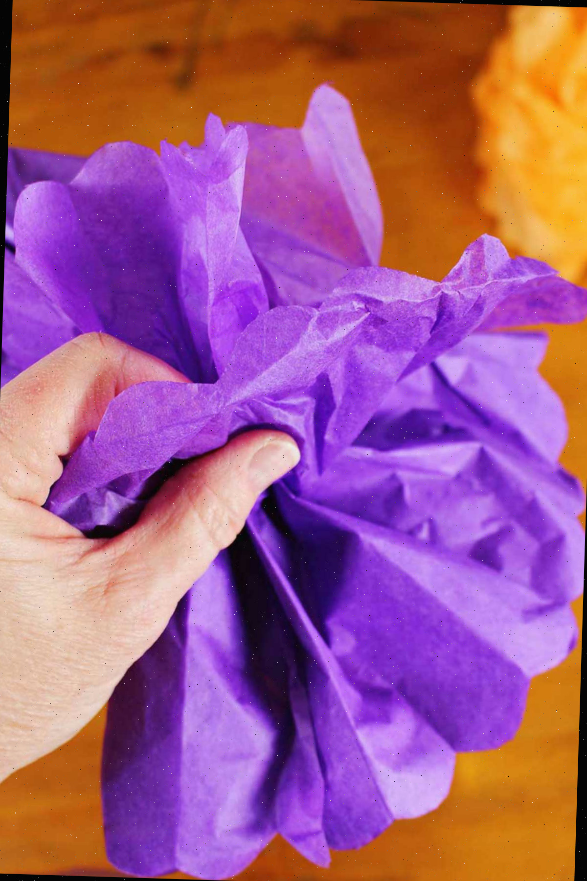 Mão desdobrando uma flor de papel de seda roxa.