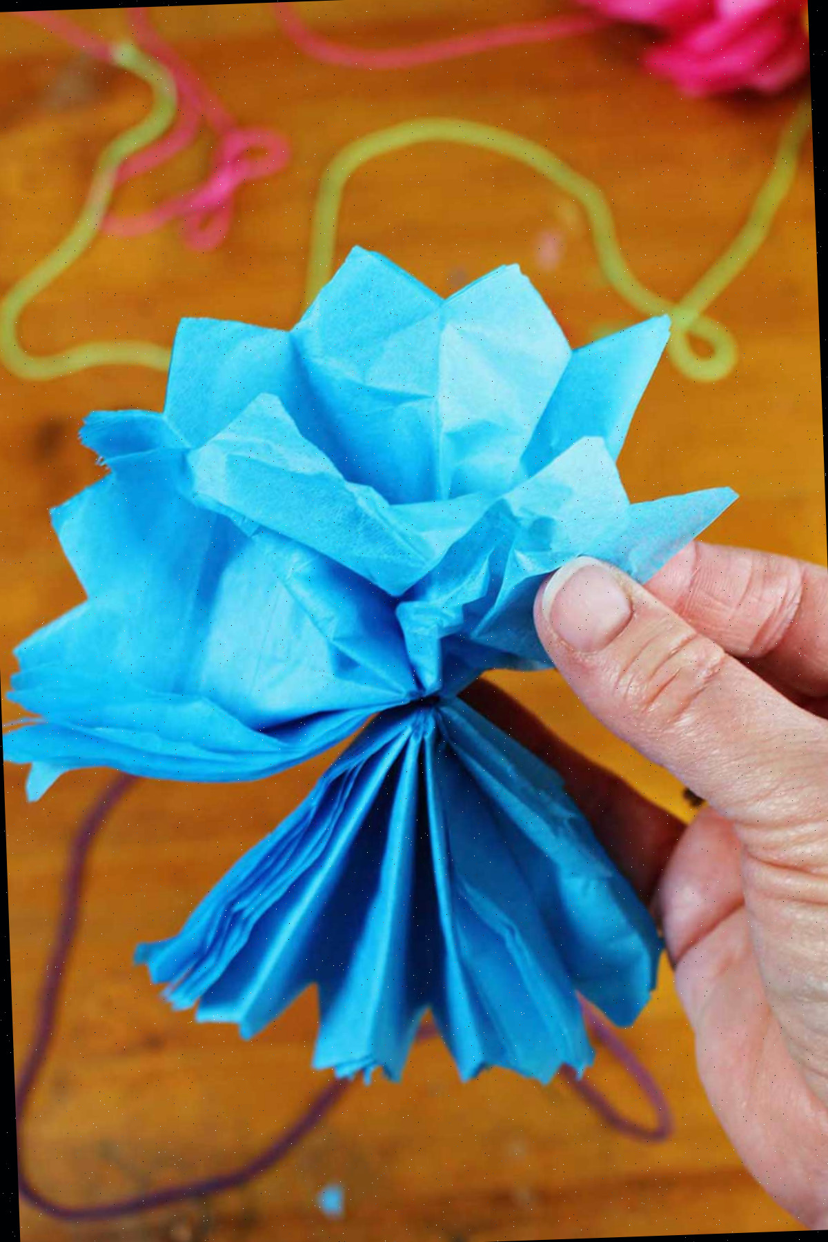 Mão abrindo e desgrenhando uma flor de papel de seda azul.