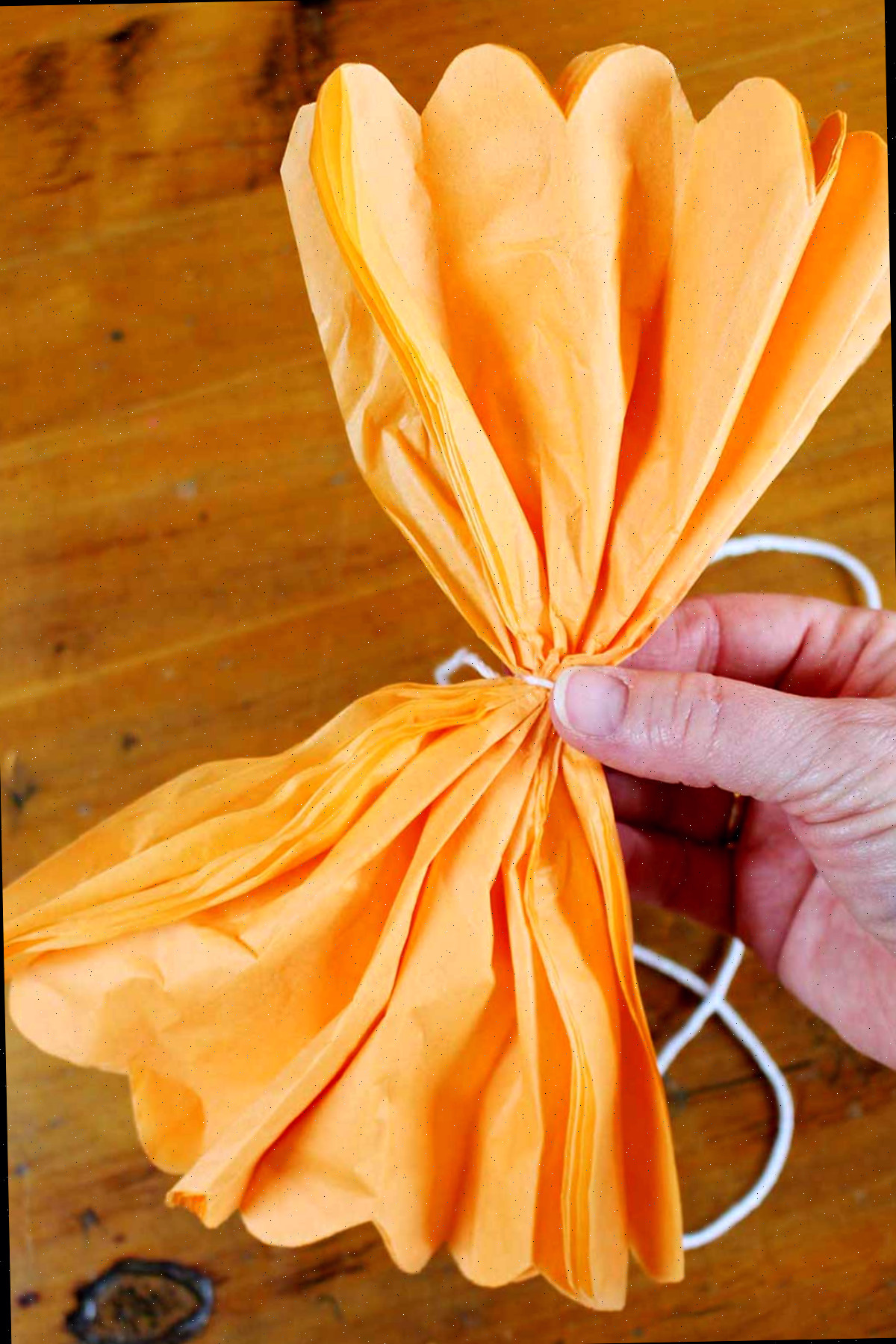 Mão segurando papel de seda laranja cortado e dobrado parcialmente aberto para mostrar a borda recortada.
